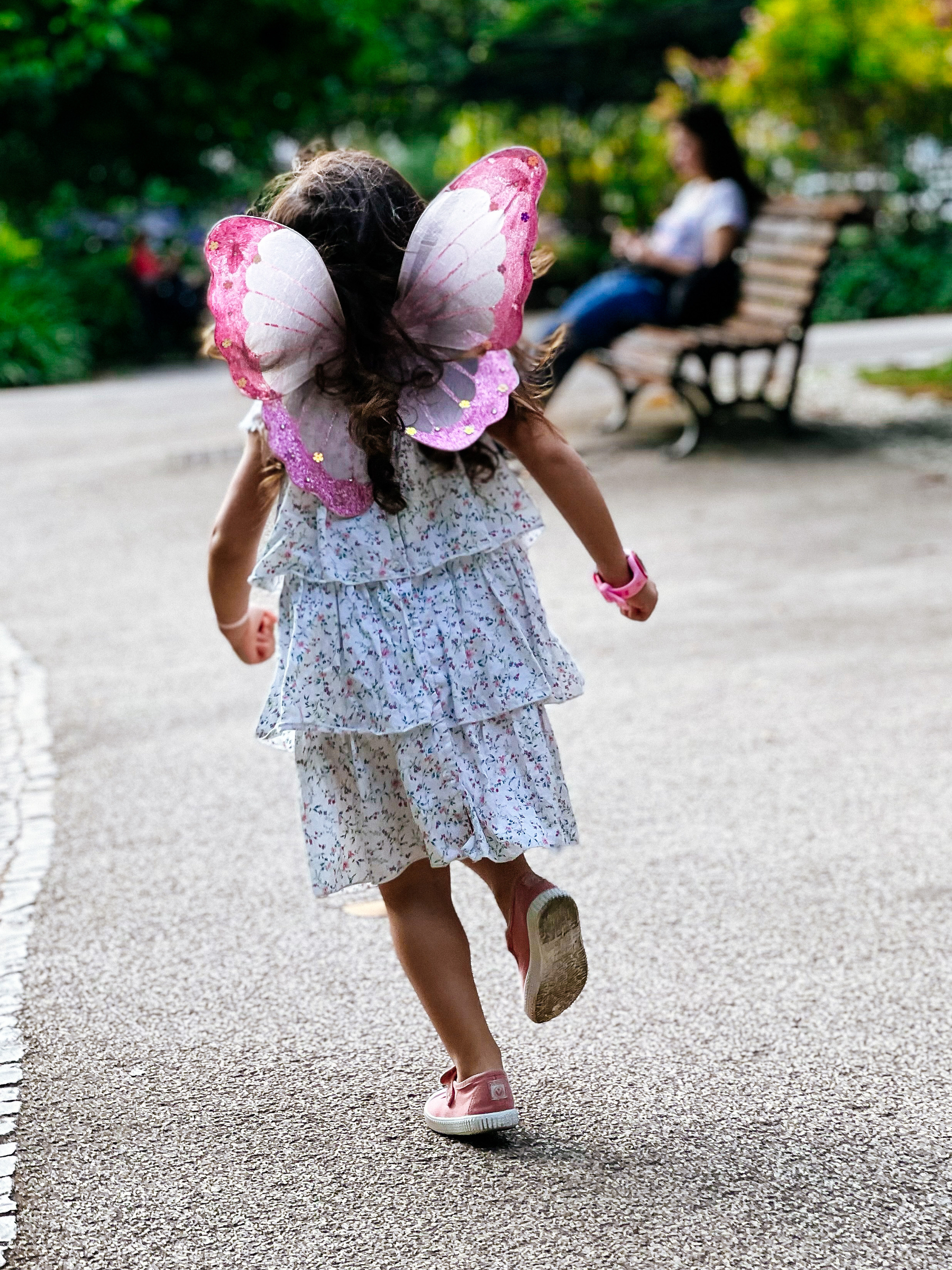A girl wearing fairy wings runs in the park. 