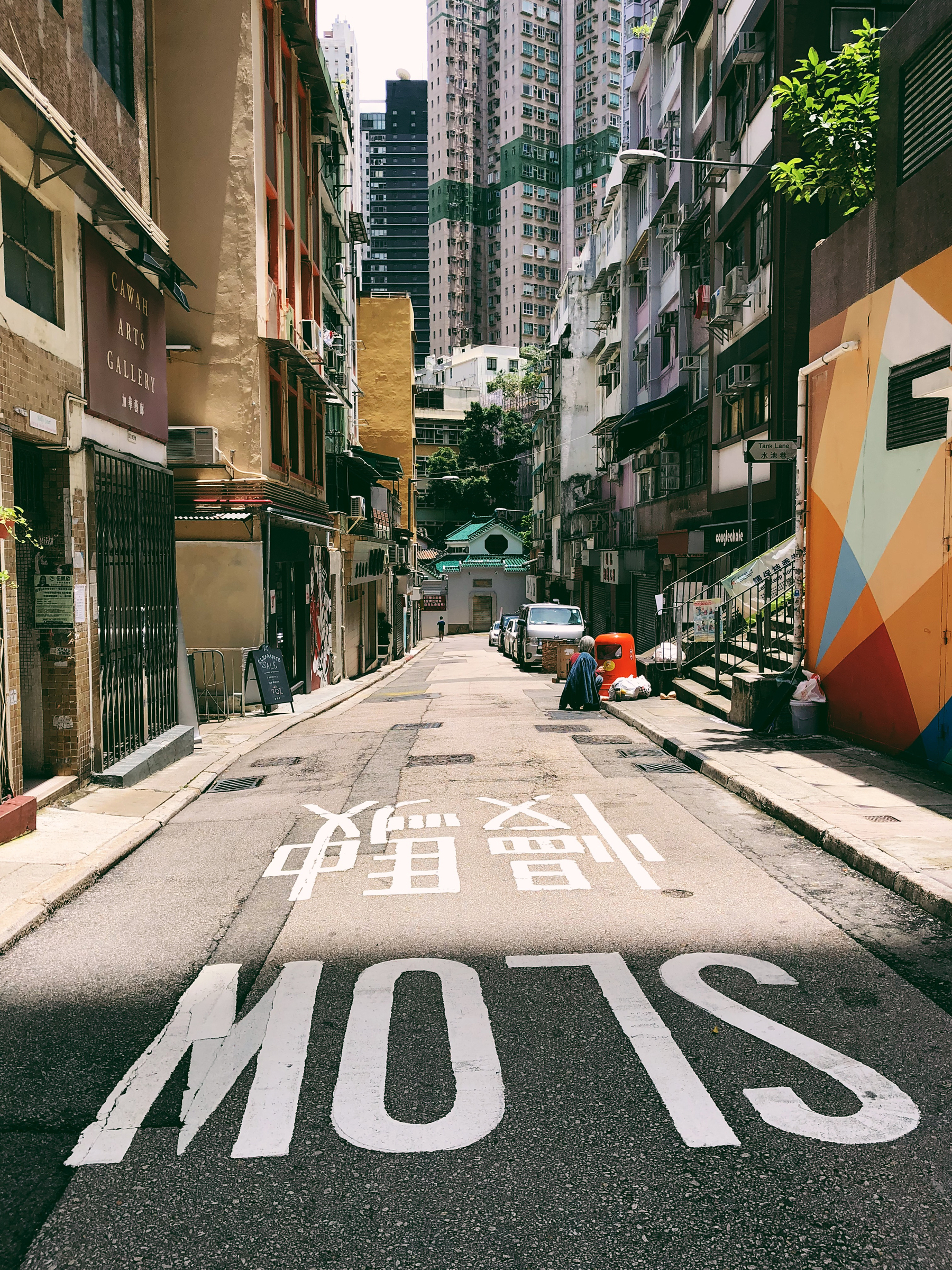 A street in Hong Kong, high rise buildings in the back, and “SLOW” written on the pavement. 