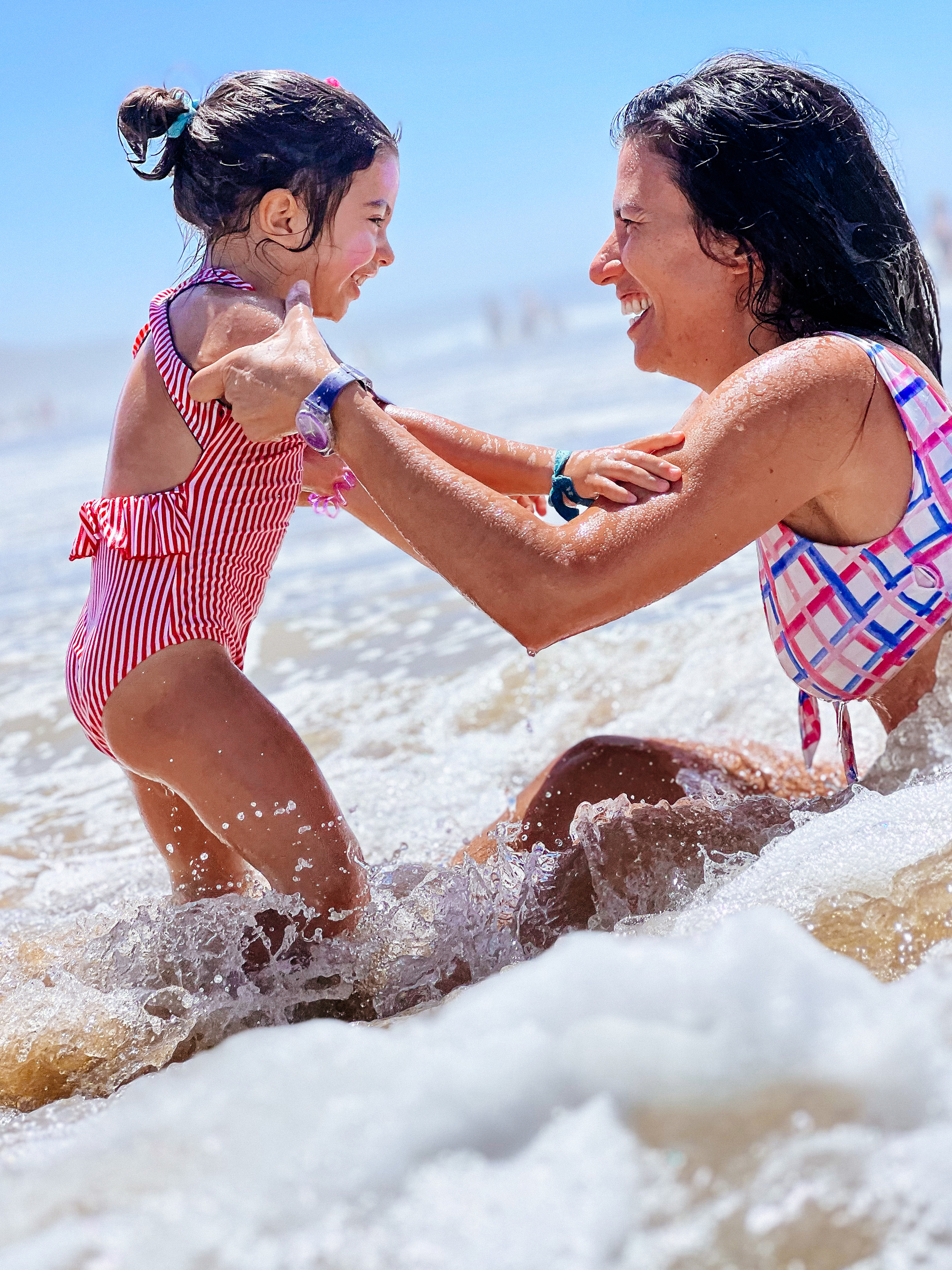 A girl and a woman play in the sea, smiling.  