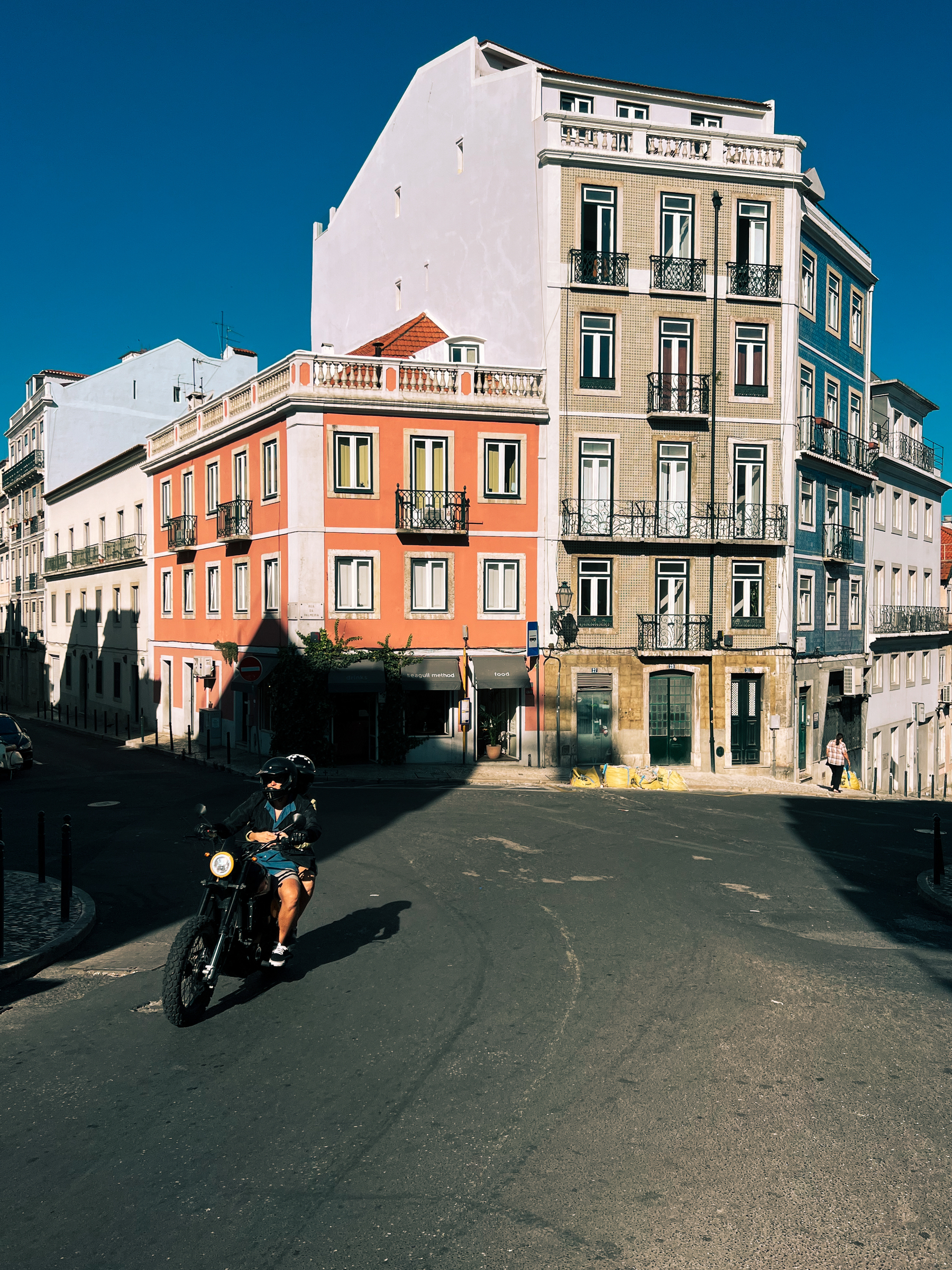 A motorcycle rides by in downtown Lisbon. Old, colorful, buildings. 