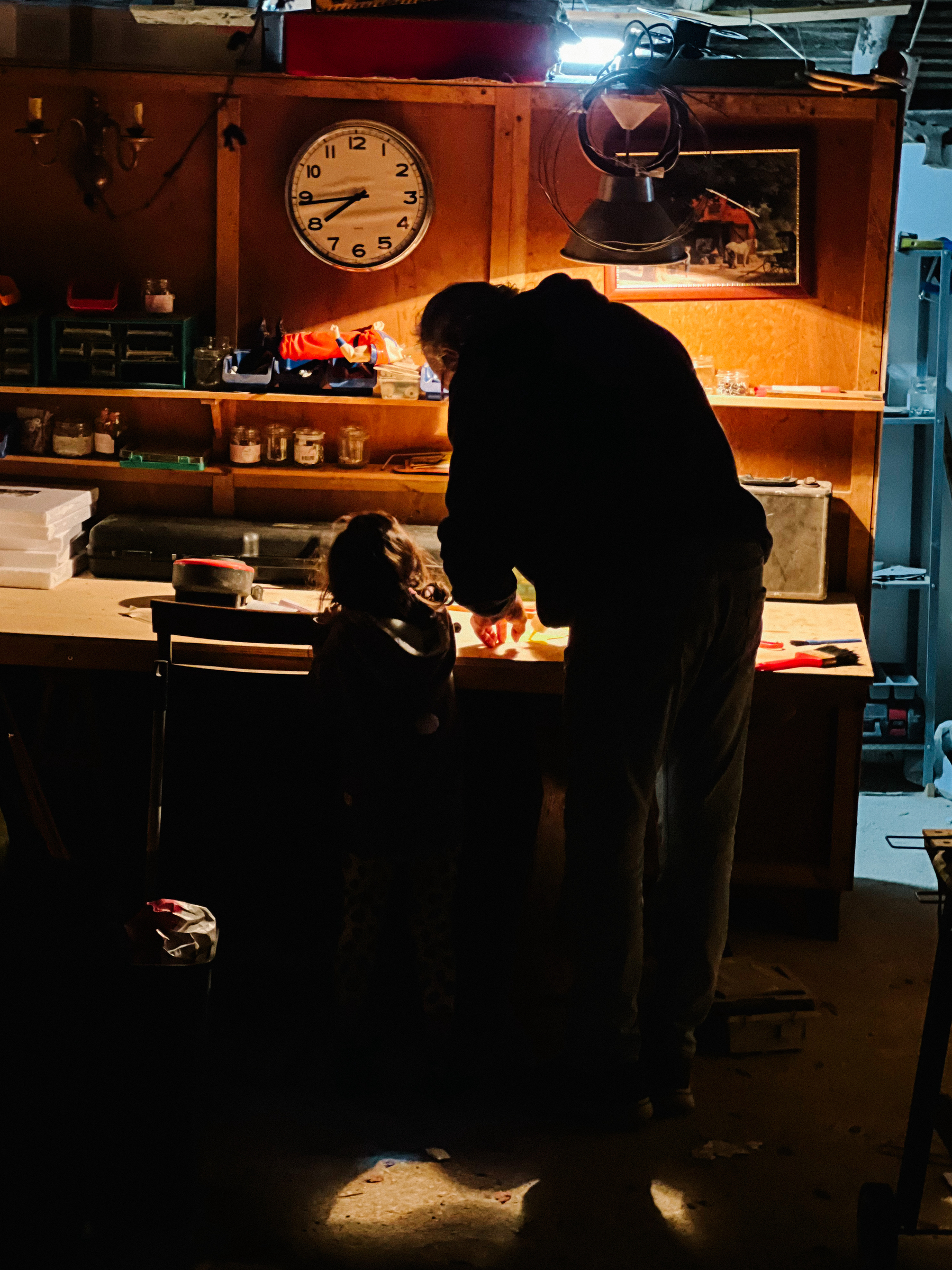 A man and a toddler with their back to us, working on something in a workbench.  