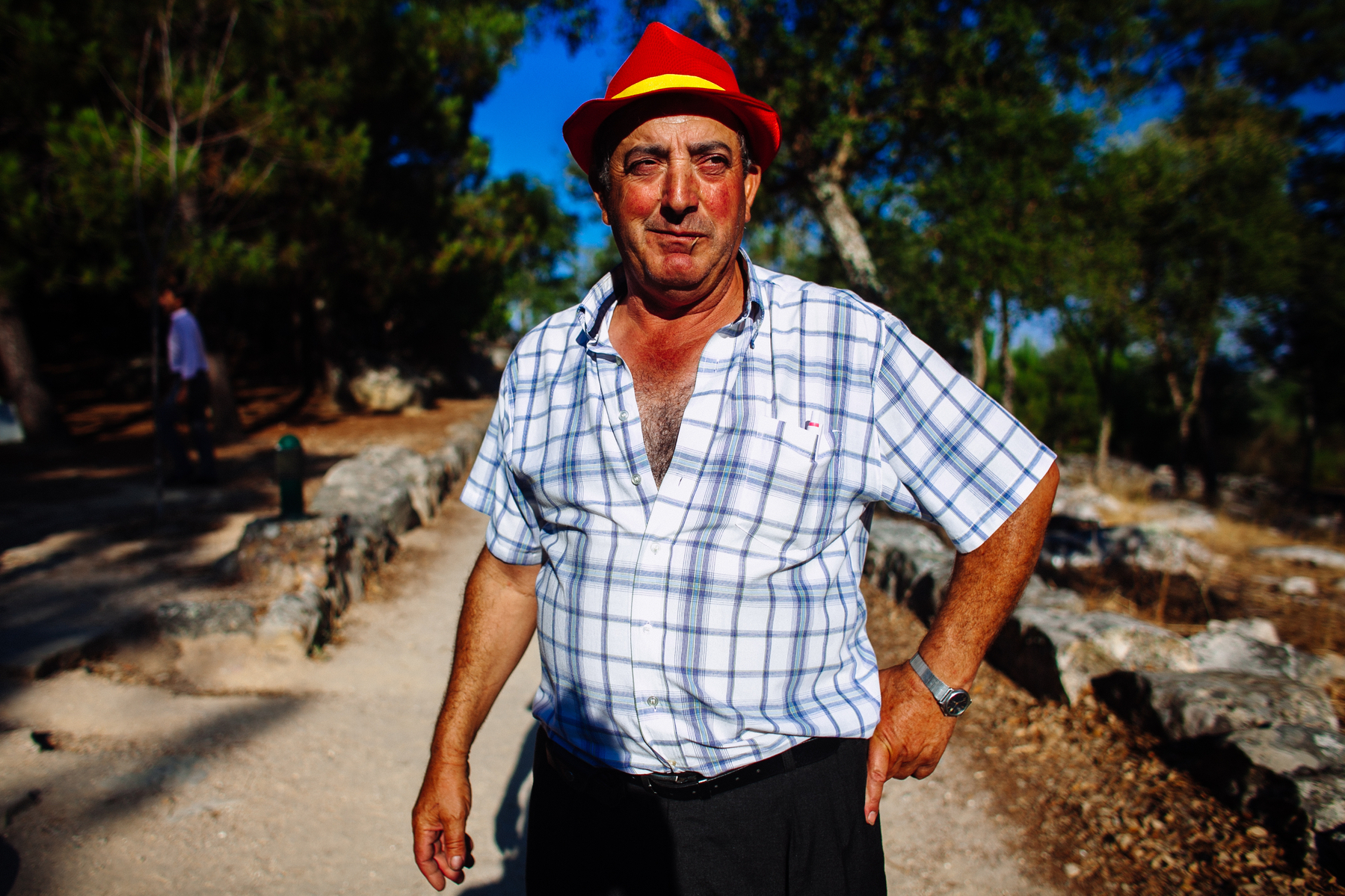 Portrait of a man with a short sleeved shirt, wearing a red hat. He’s outdoors. 