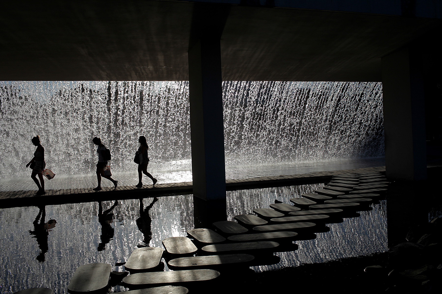 Three people walking on a path under a man-made waterfall.
