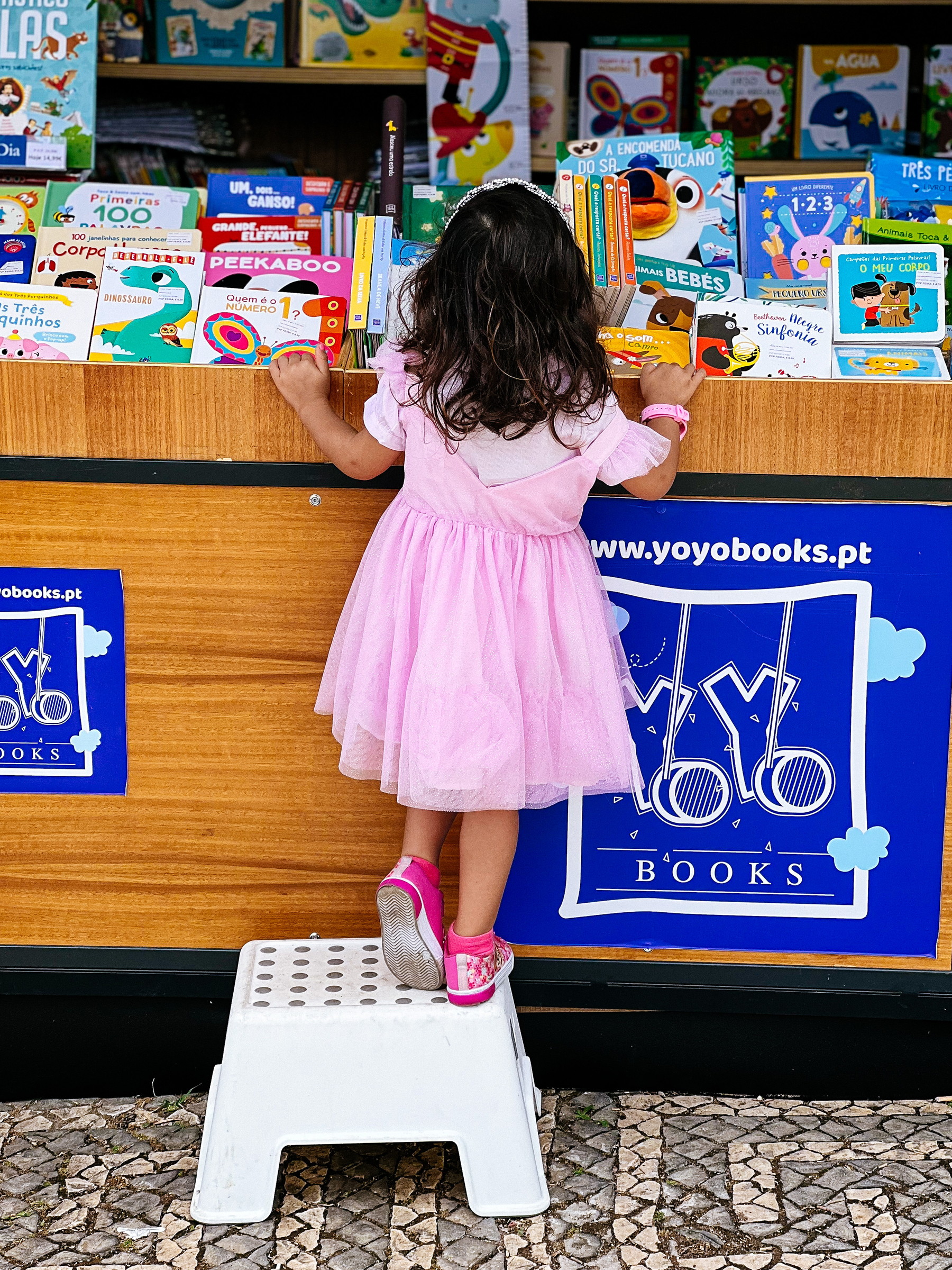a girl stands on a stool, looking at a book stand