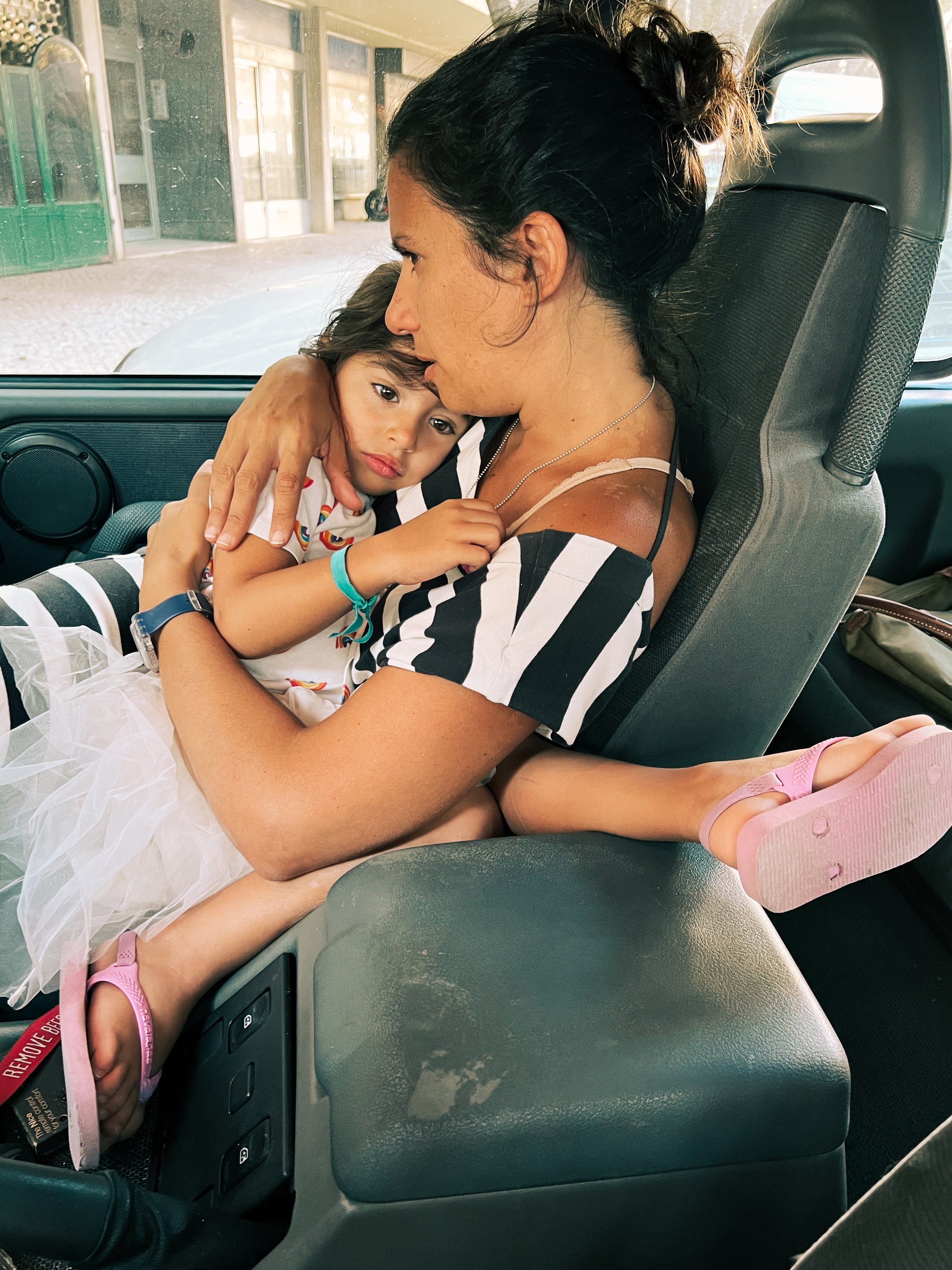 Mother and daughter, holding each other, sitting inside a car. 
