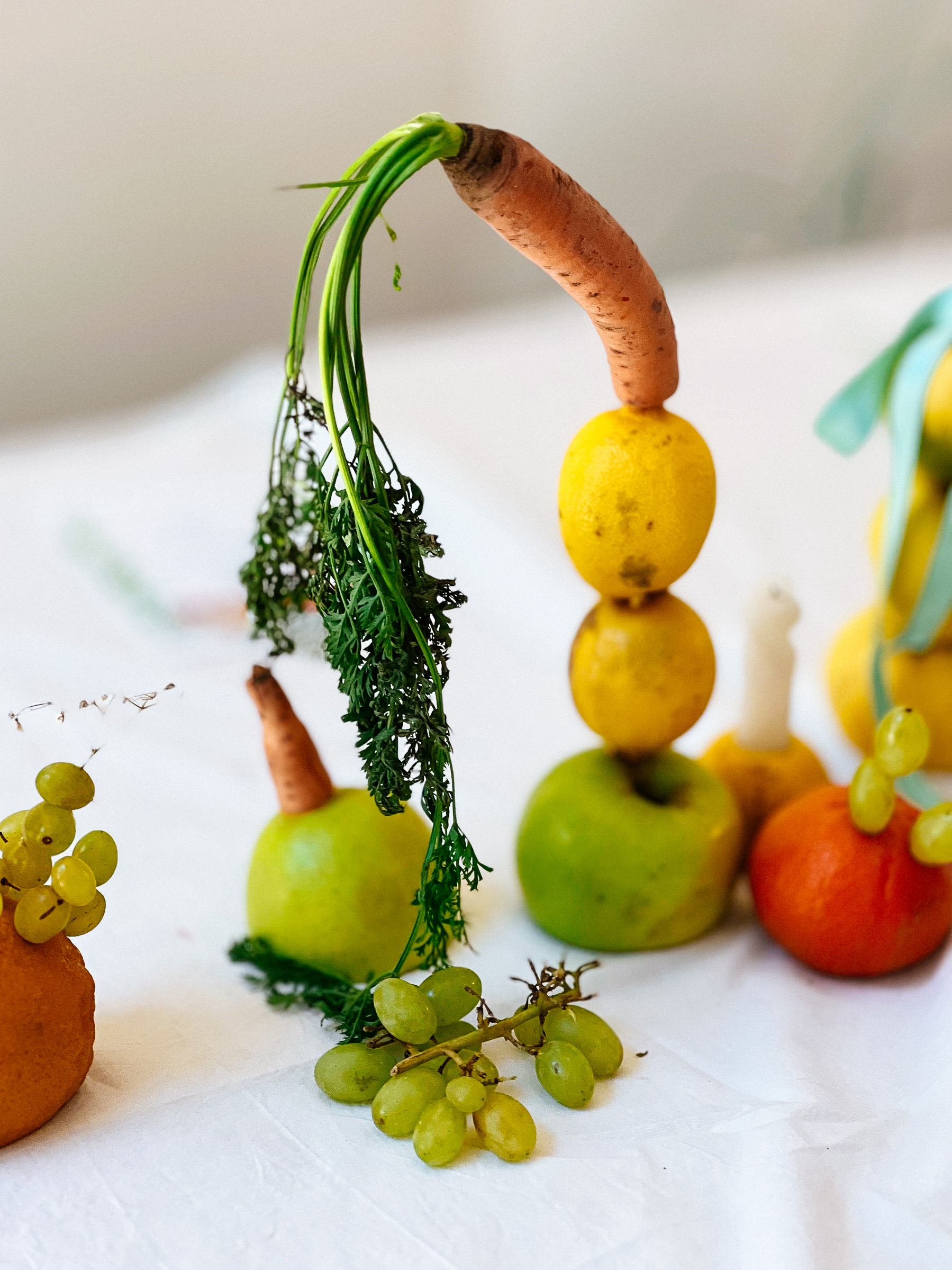 A carrot and some apples, arranged, like a sculpture. Some grapes as well. 