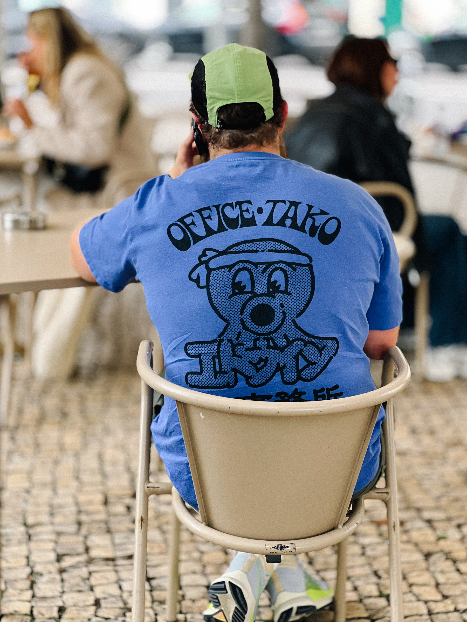 An hipster, complete with cycling cap, sits at a cafe, wearing an &ldquo;office-tako&rdquo; t-shirt, from Edwin.