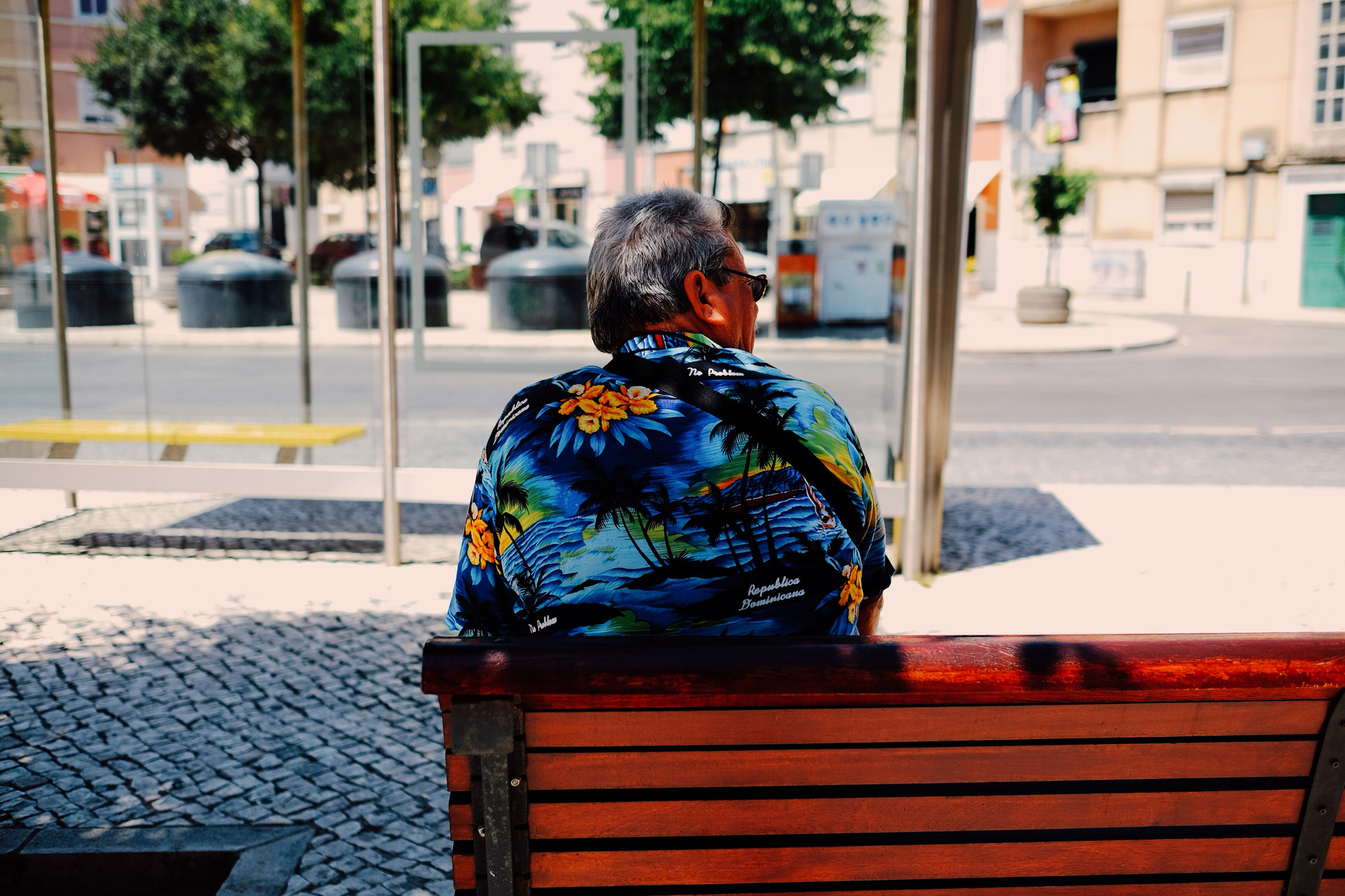 a man with a very colourful shirt sitting in a bench.