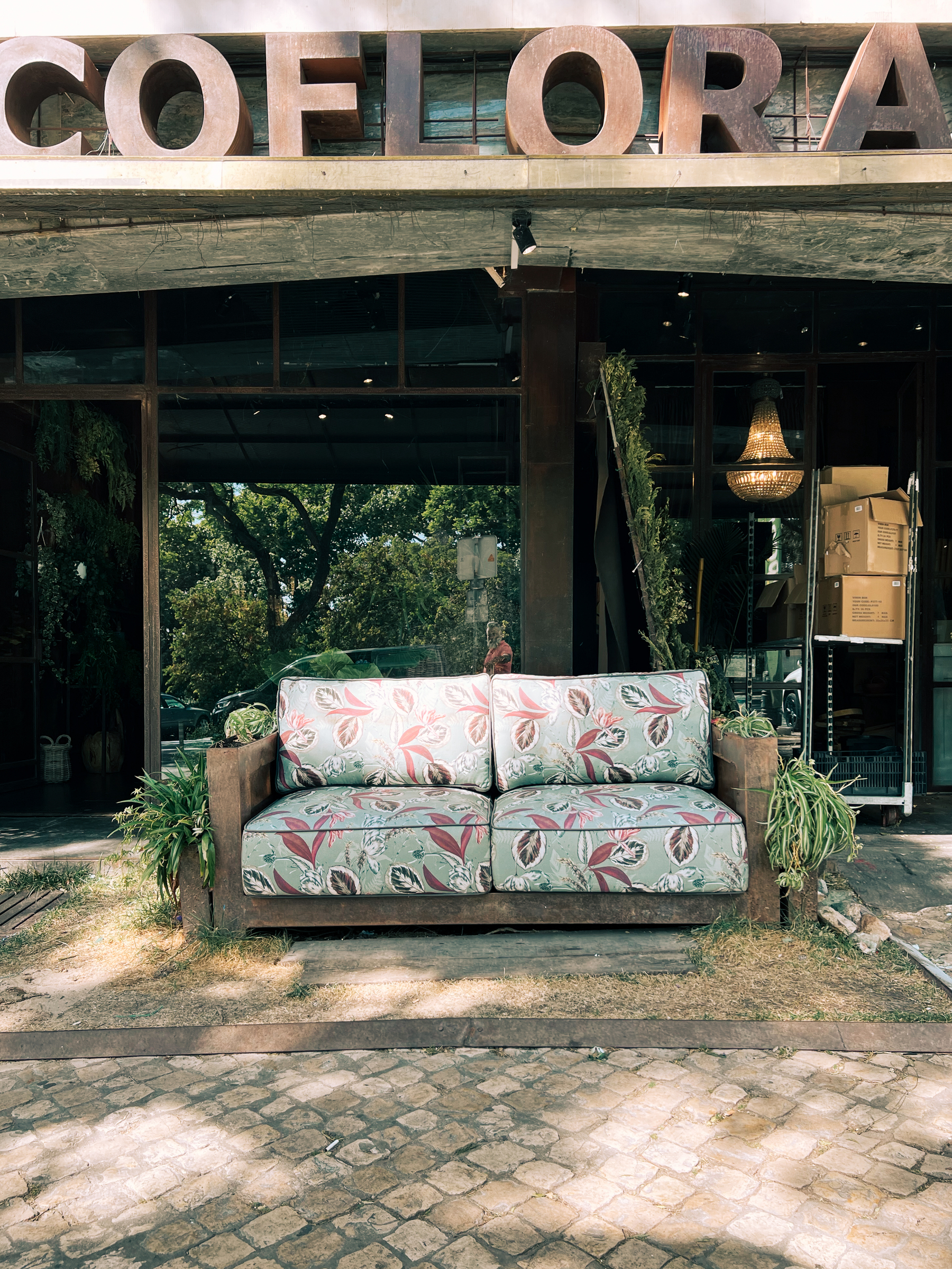 A sofa sits outside, in front of a flower shop.
