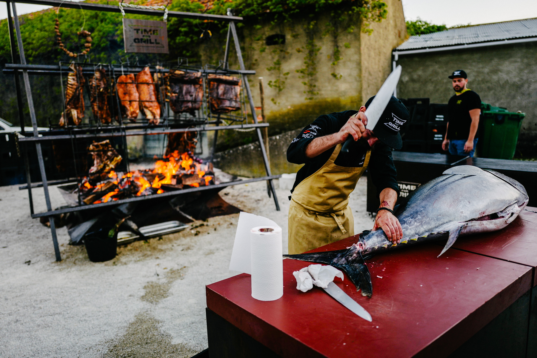 A chef prepping a tuna, barbecue in the back. 