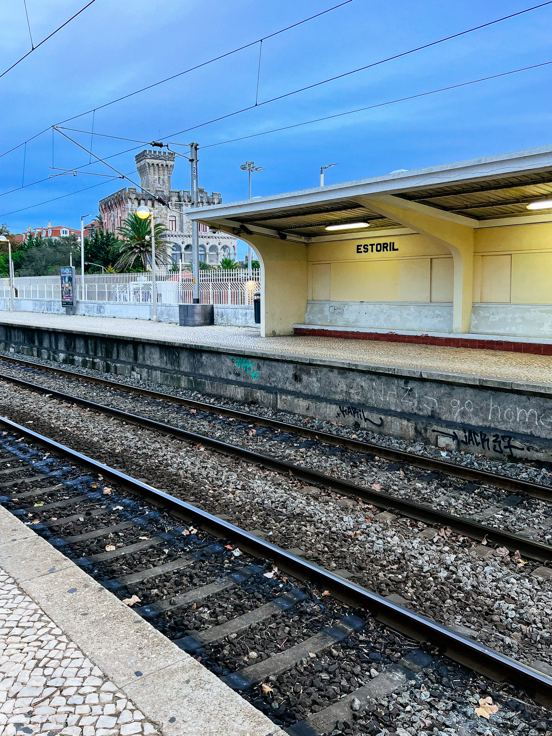 A tiny castle in the distance, train tracks on the foreground. Estoril train station. 