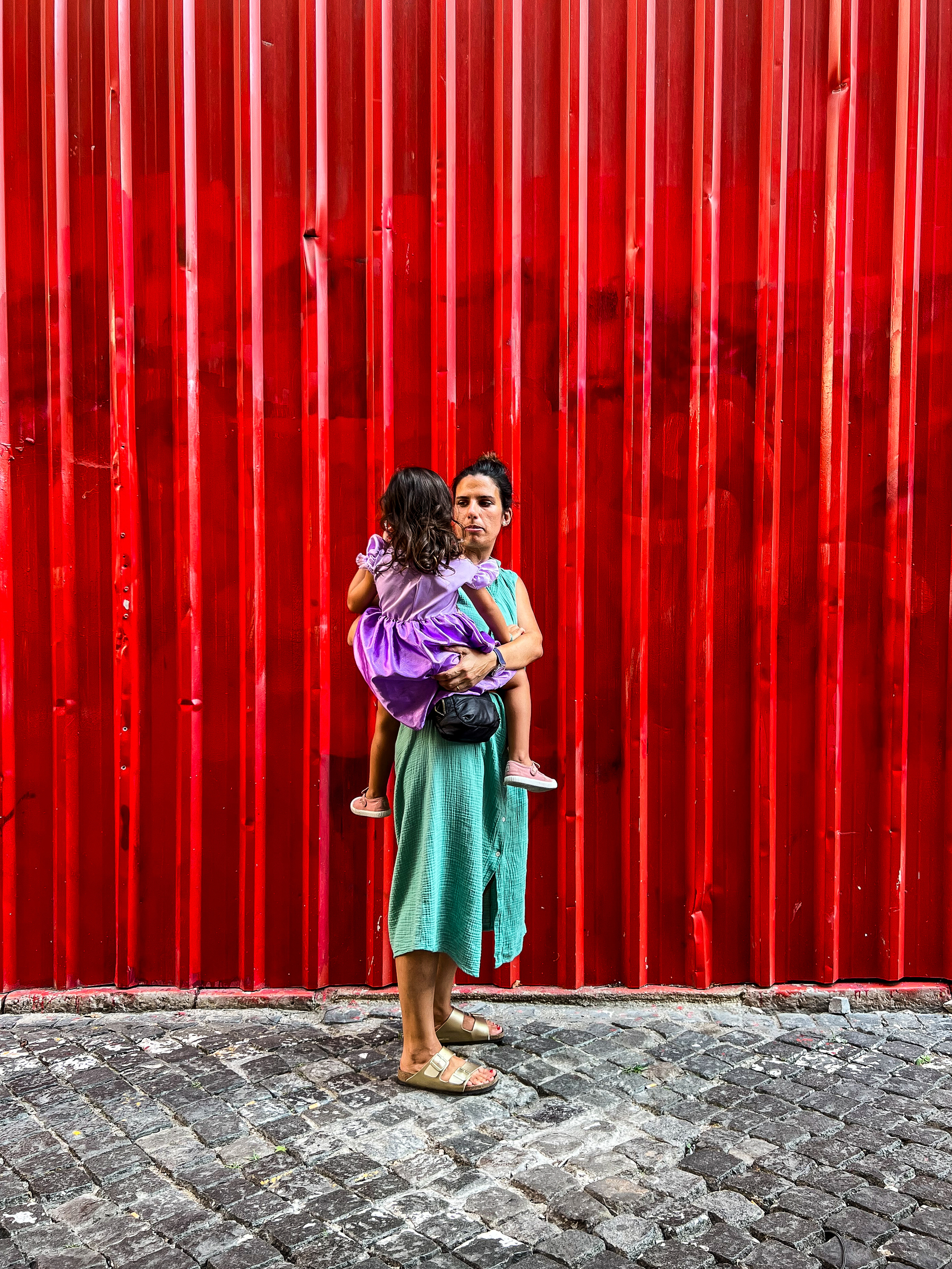 a woman holds a toddler, red wall in the background.