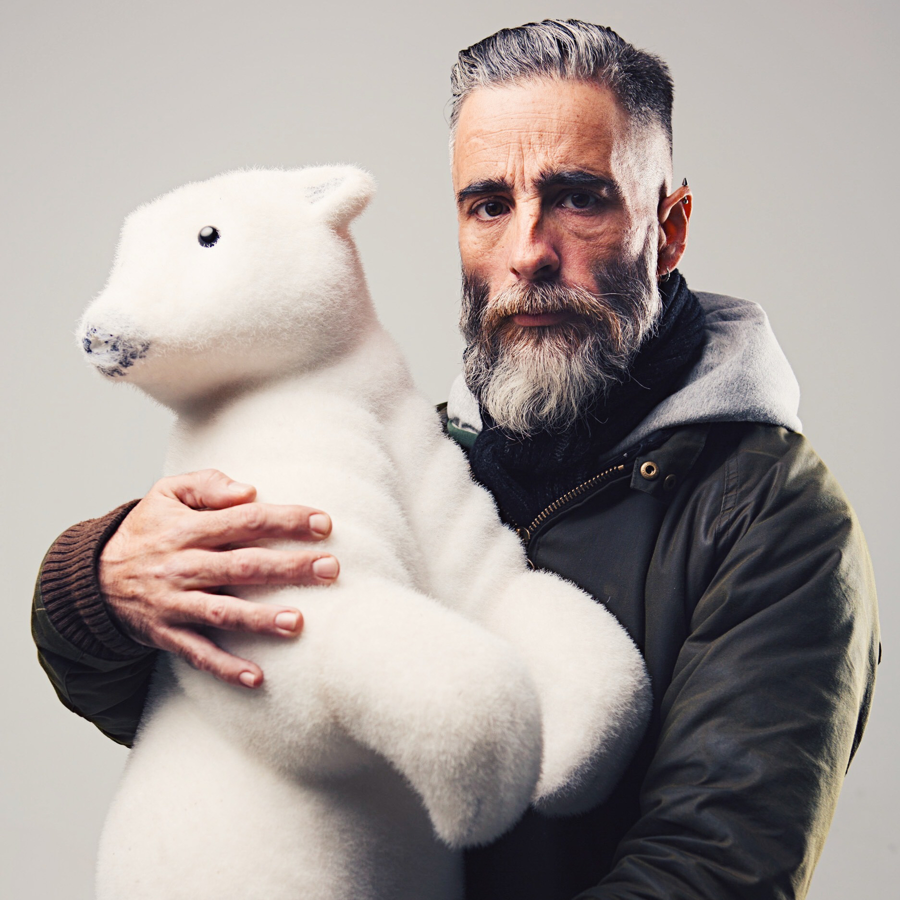 Bearded man holding a toy white bear. 