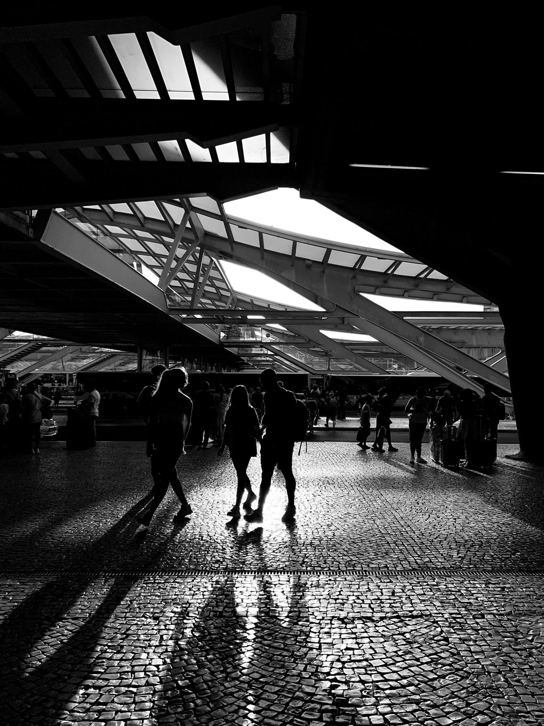 Black and white photo, people walk by a modern looking structure. 