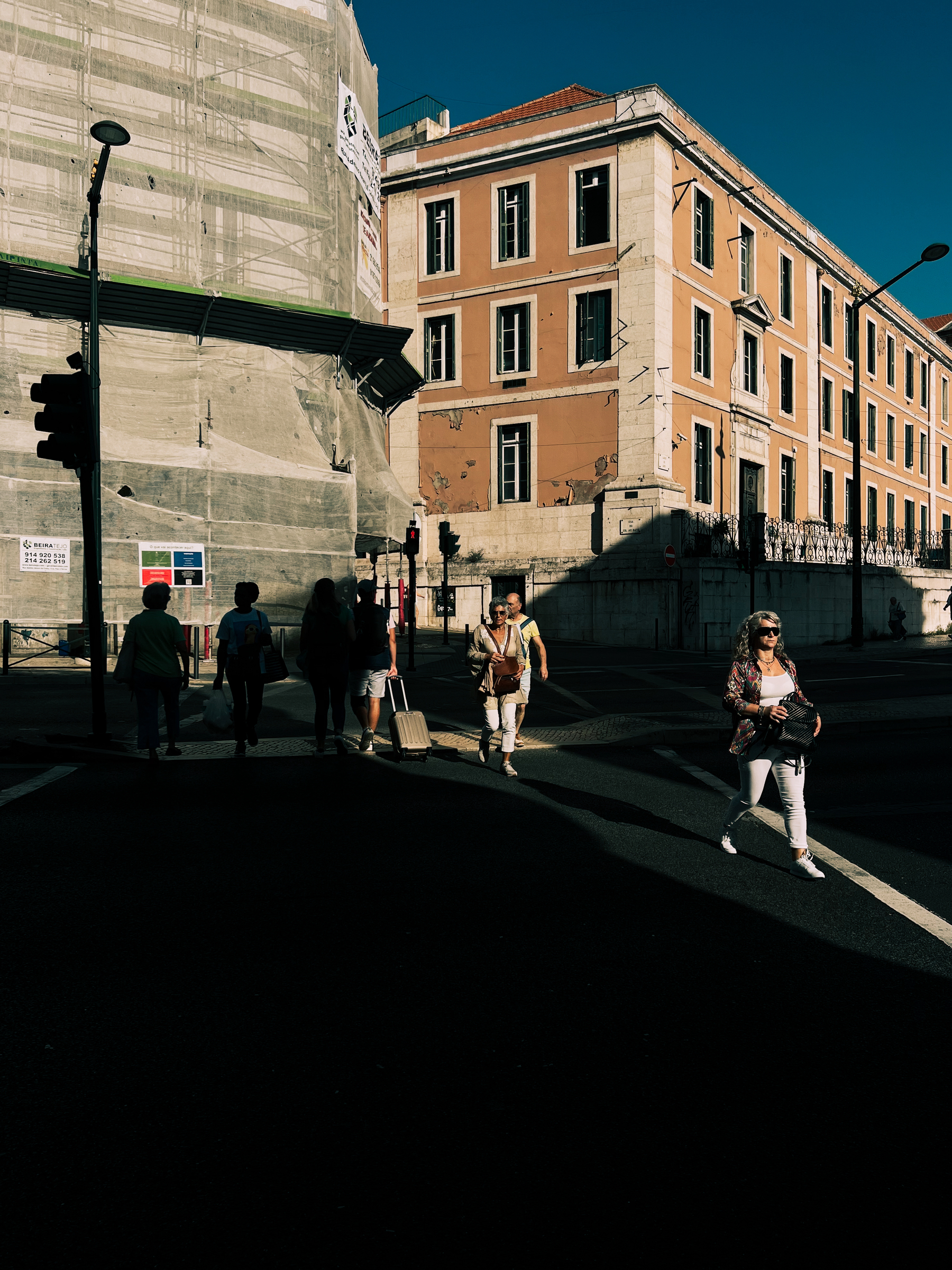 People crossing the street, shaded corner. 
