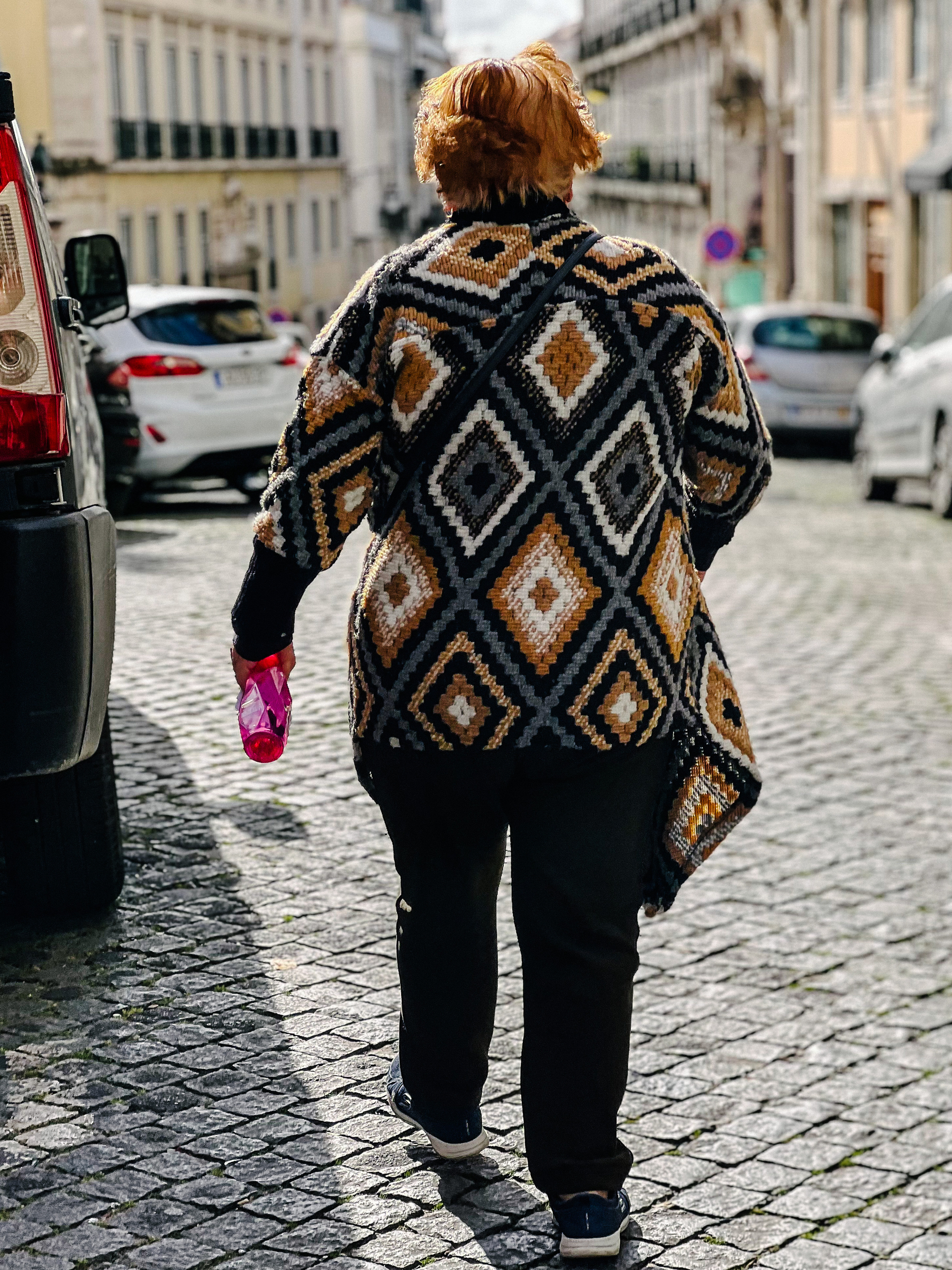 A woman walking in front of us, with a pink bottle in her hand. 