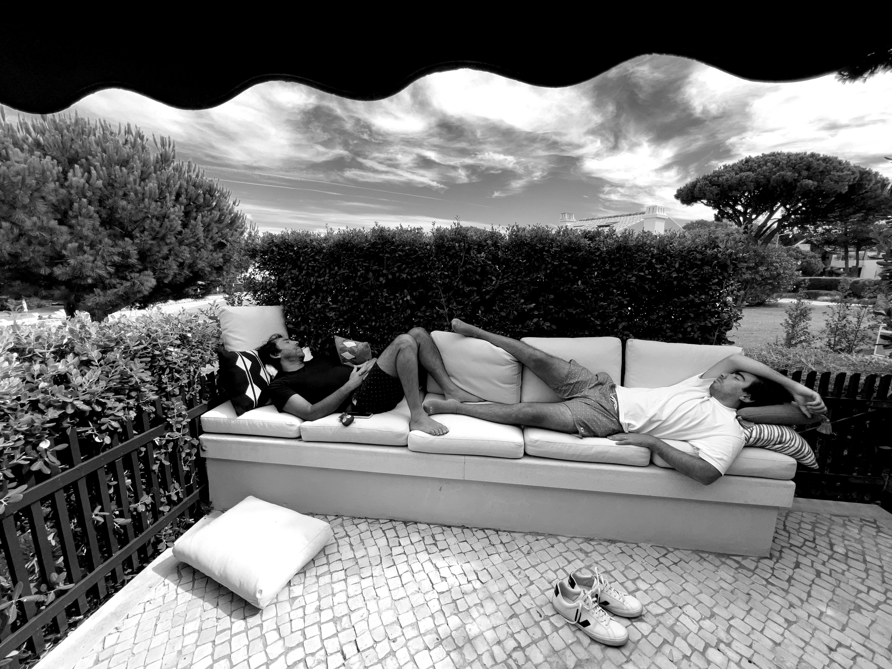 Black and white photo of two men sleeping in a sofa, outside. 