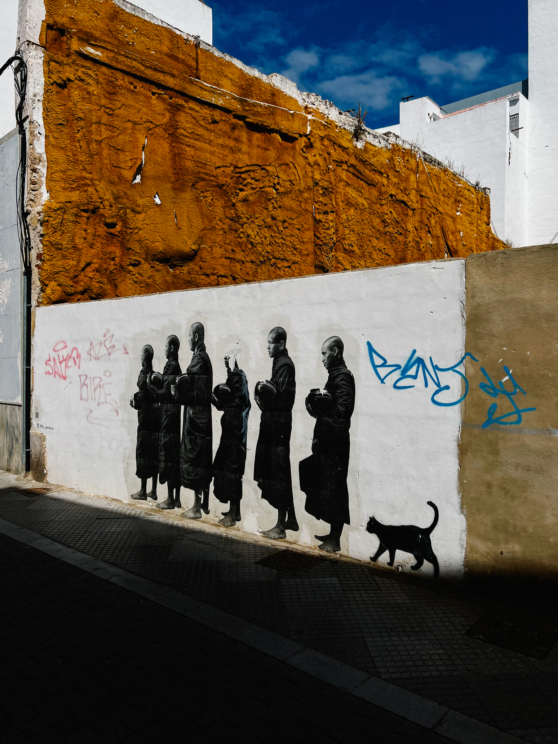 A street art piece, monks in a row, and a cat following them. 