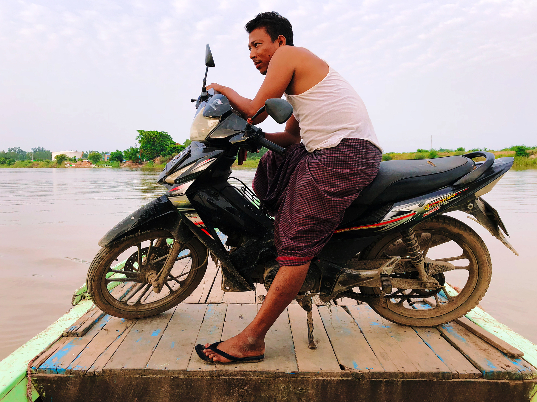 A man looks out at the distance, sitting on his motorcycle, while riding on a boat. 