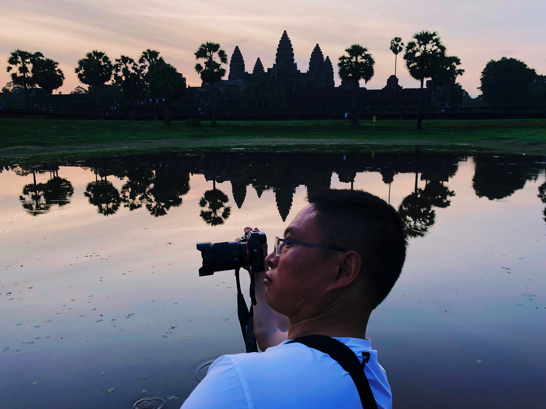 Sunrise over Angkor Wat. A man holds a camera in the foreground, the temple’s skyline in the background. 