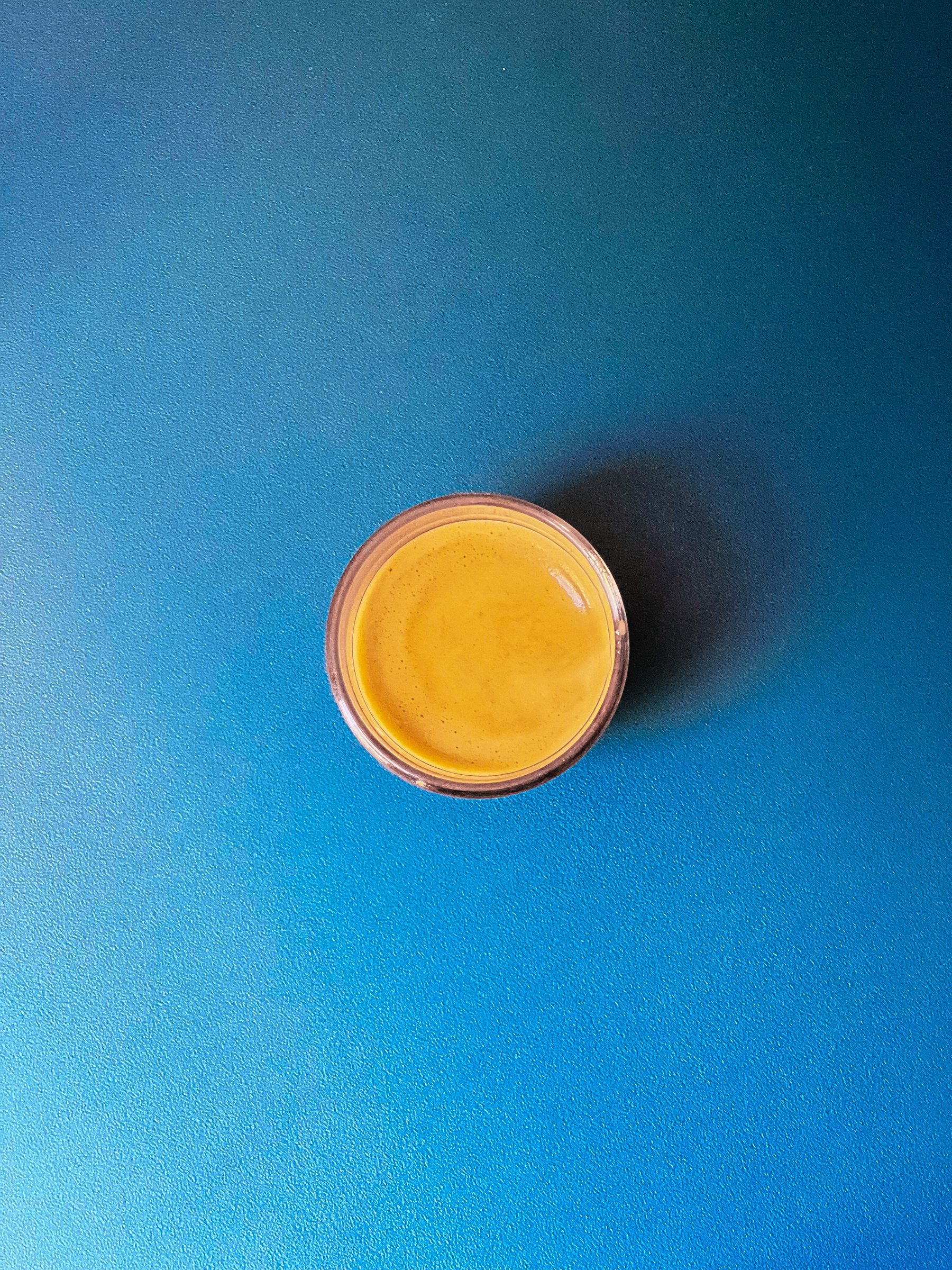 An espresso sits on a blue surface. Shot from above. 