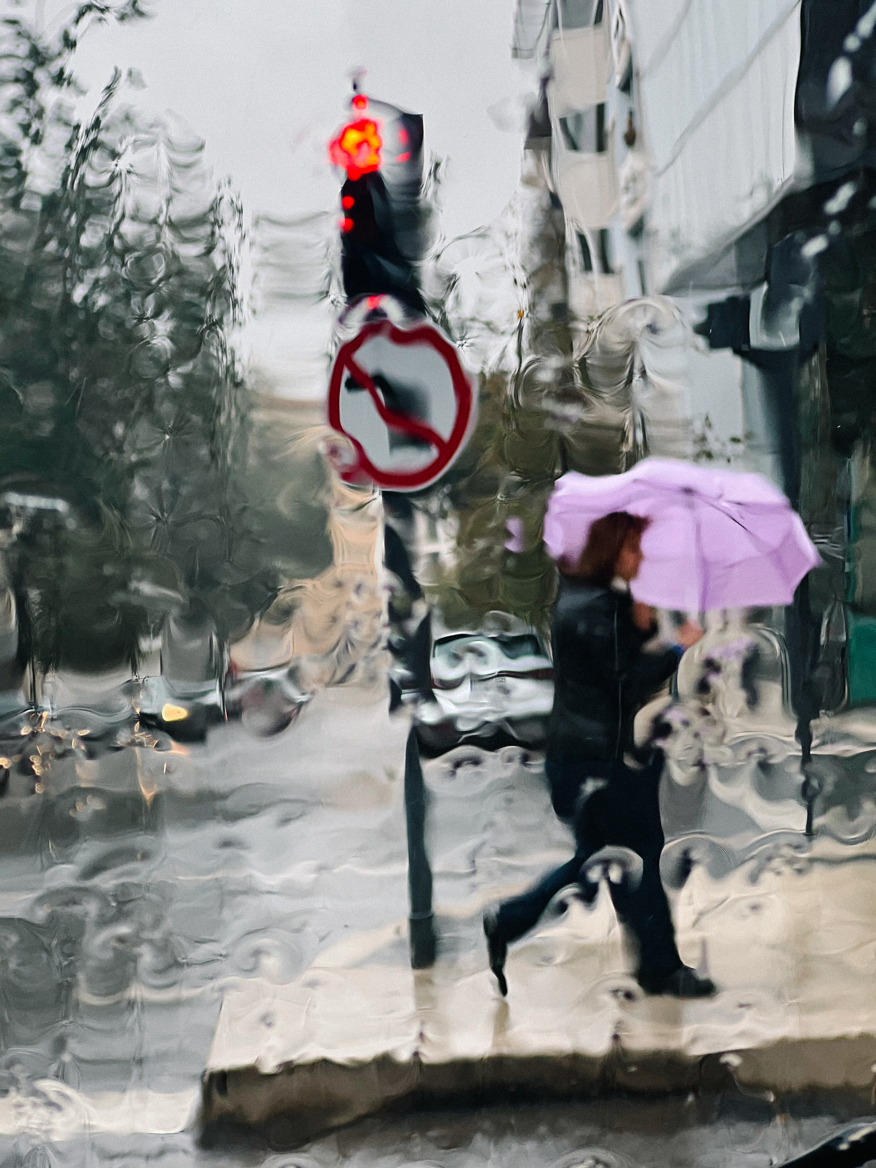 A woman crosses the road with an umbrella. Seen from inside a car. 