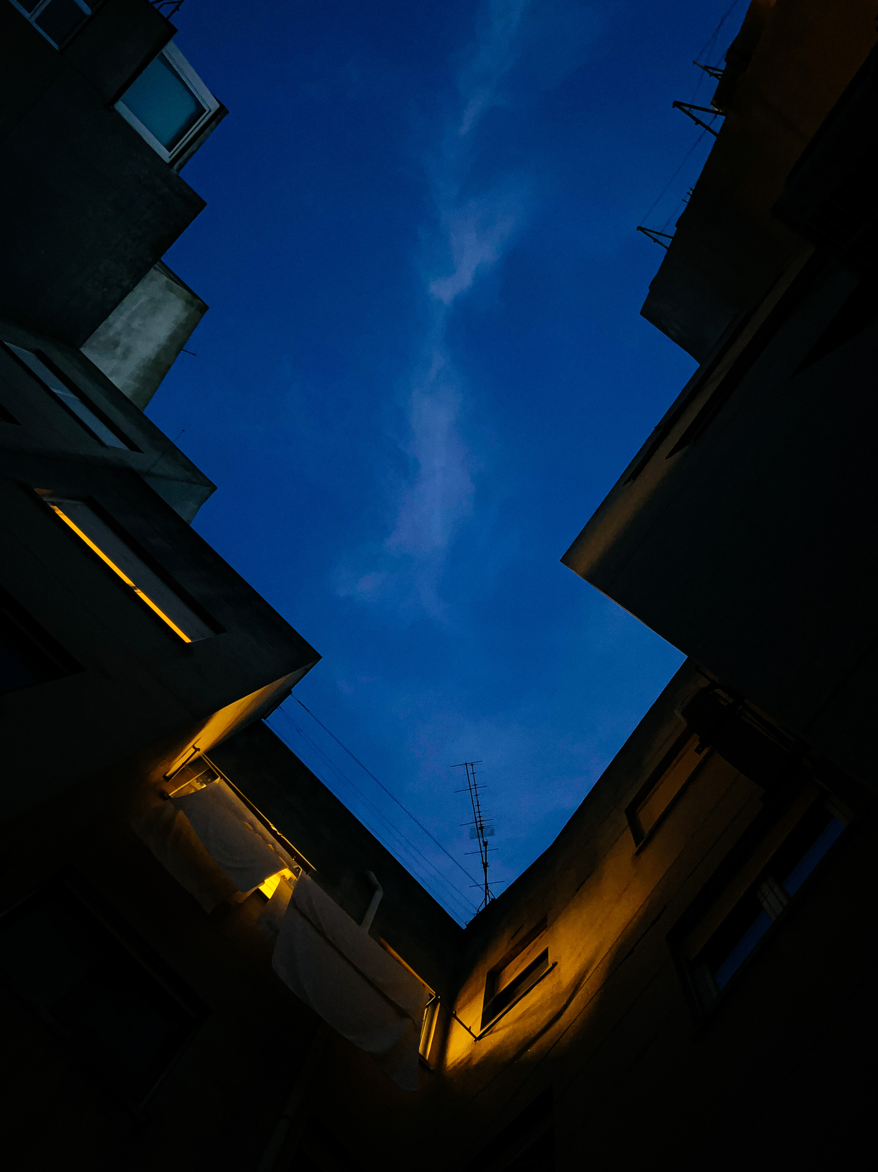Looking up, right after sunset. Dark blue sky, framed by a building. Some of the windows have light coming out. 