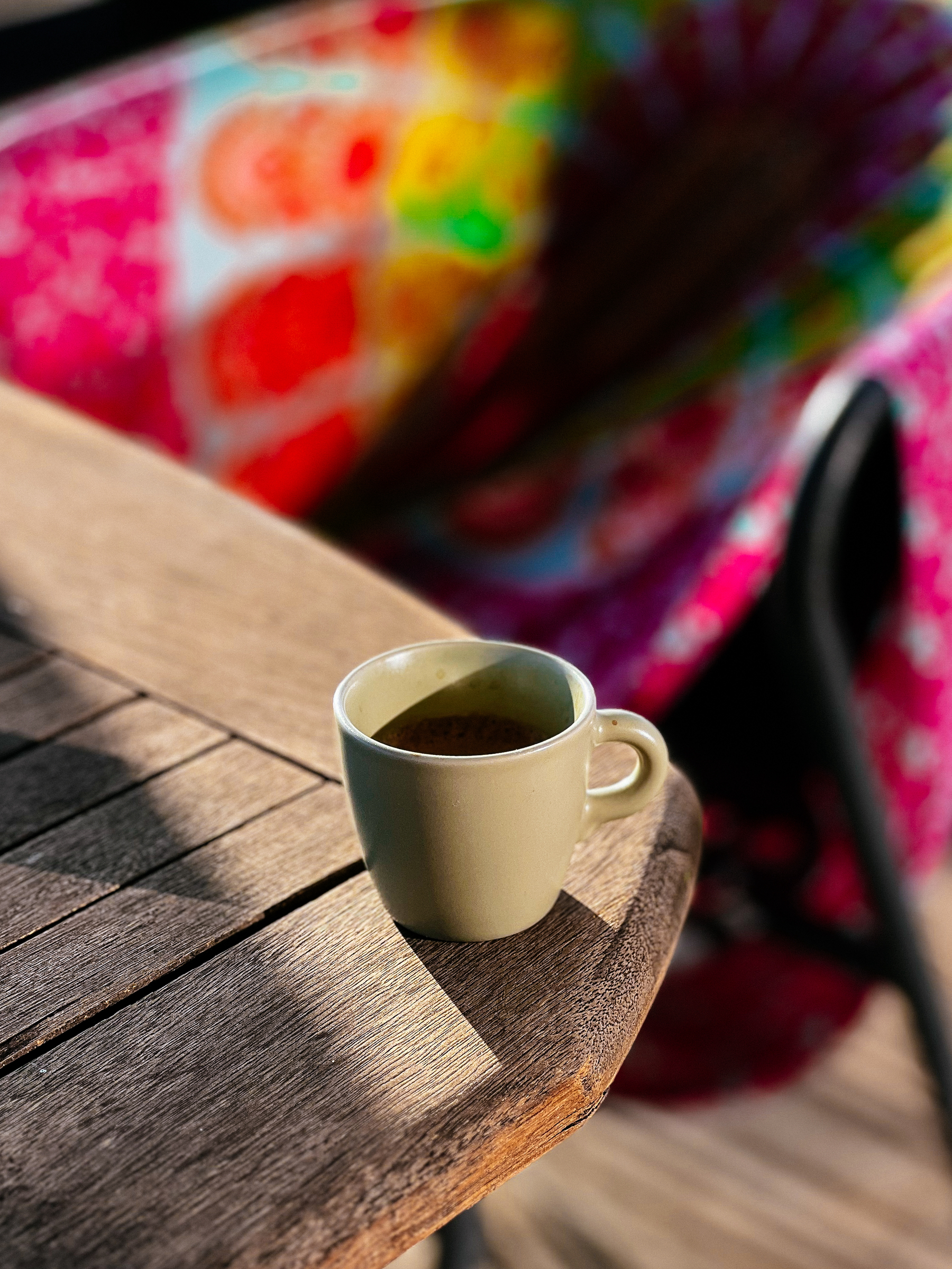 An espresso cup on a table, with a colorful sarong in the back. 