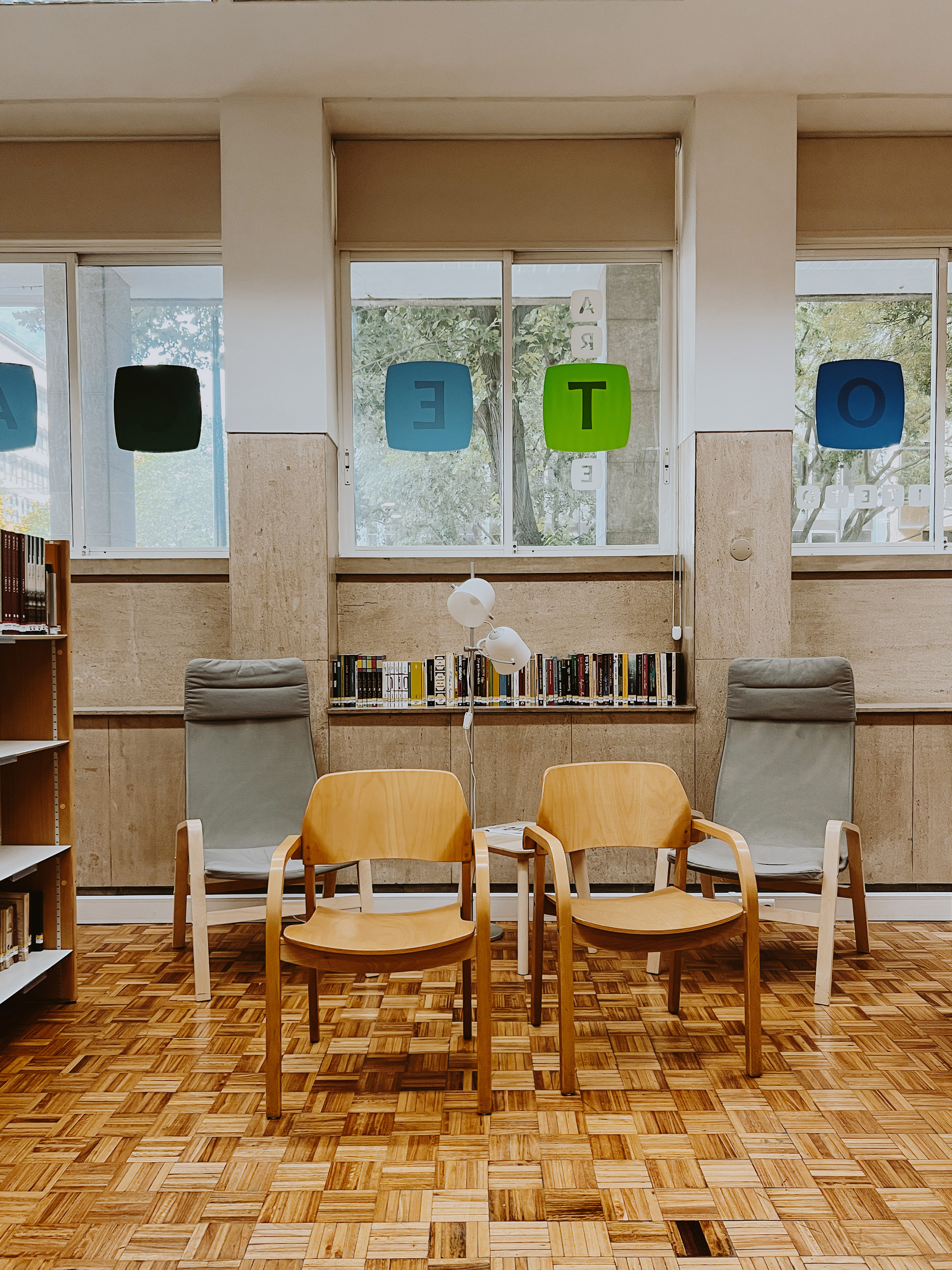 Empty chairs on a wooden floor. A bookshelf on the left side. 