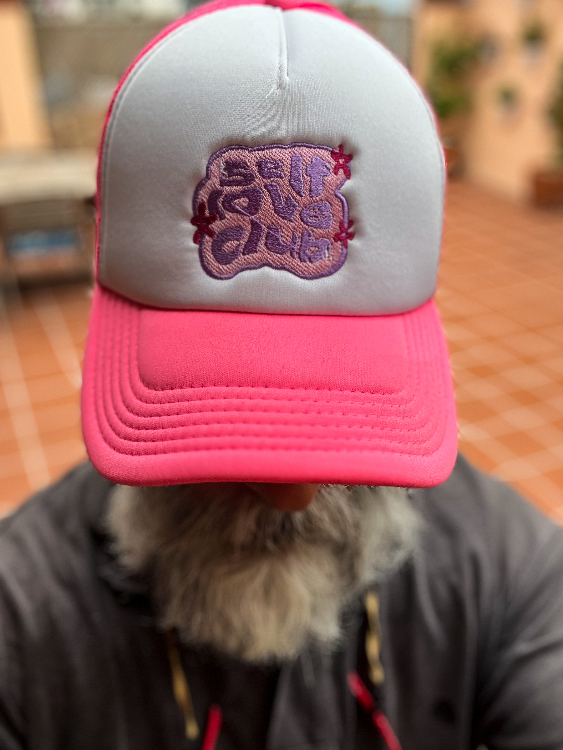 Man wearing a pink trucker hat, with “self love club” embroidery. 