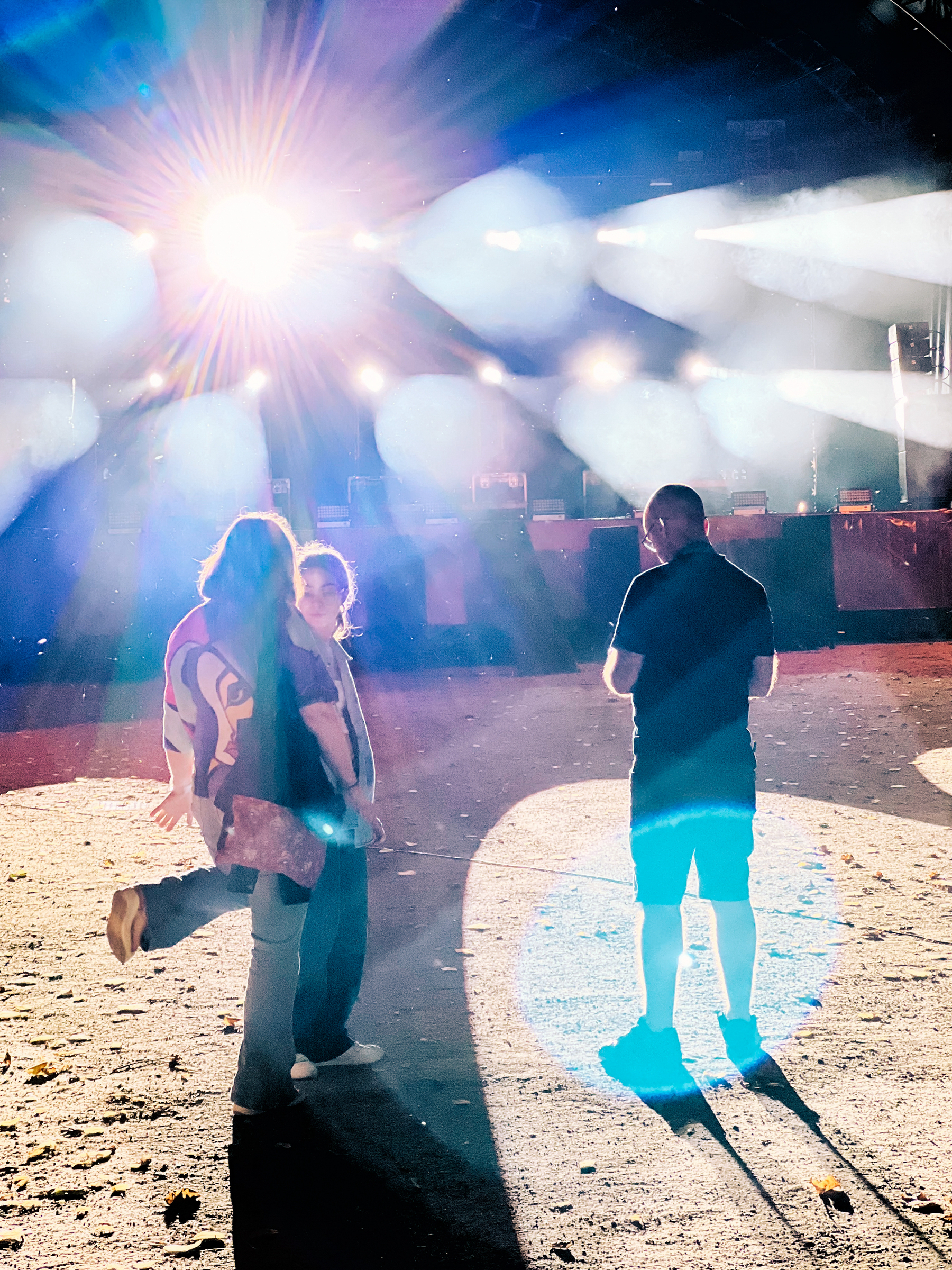 Three people standing in front of an impressive light show coming from a stage.