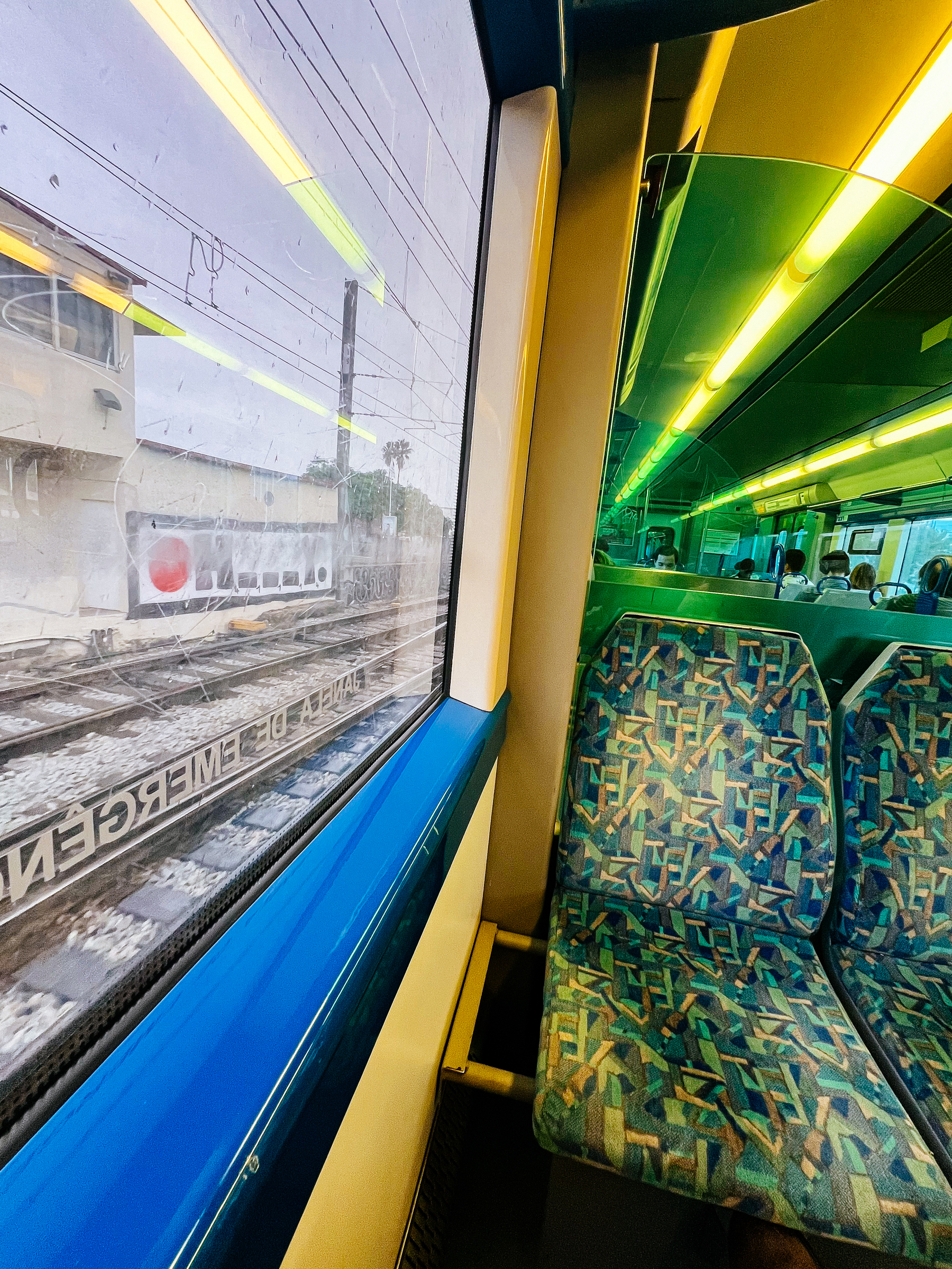 Shot from inside a train, buildings outside, and a colorful seat inside. 