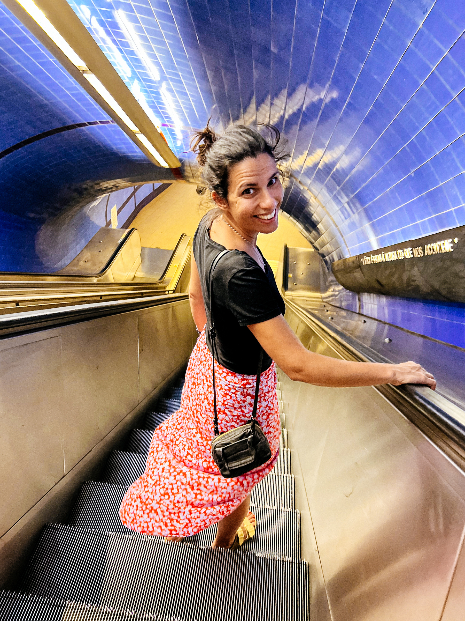A woman going down an escalator, looking back at us, beautiful smile on her face. 