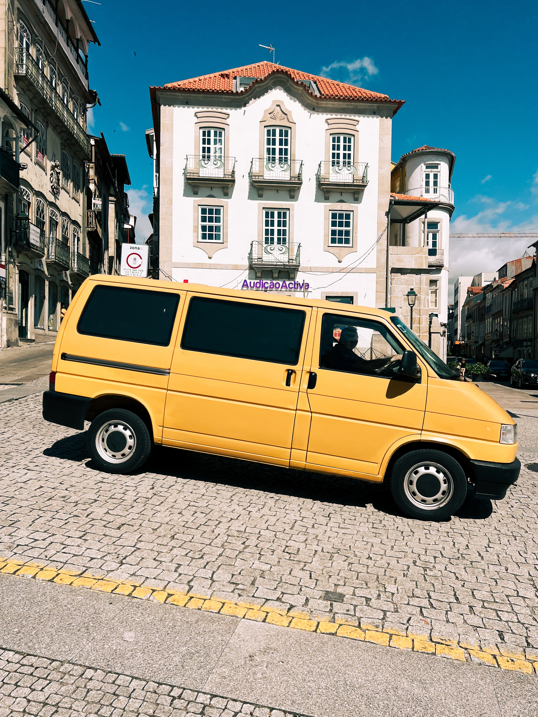 A yellow van drives by a classic looking building. 