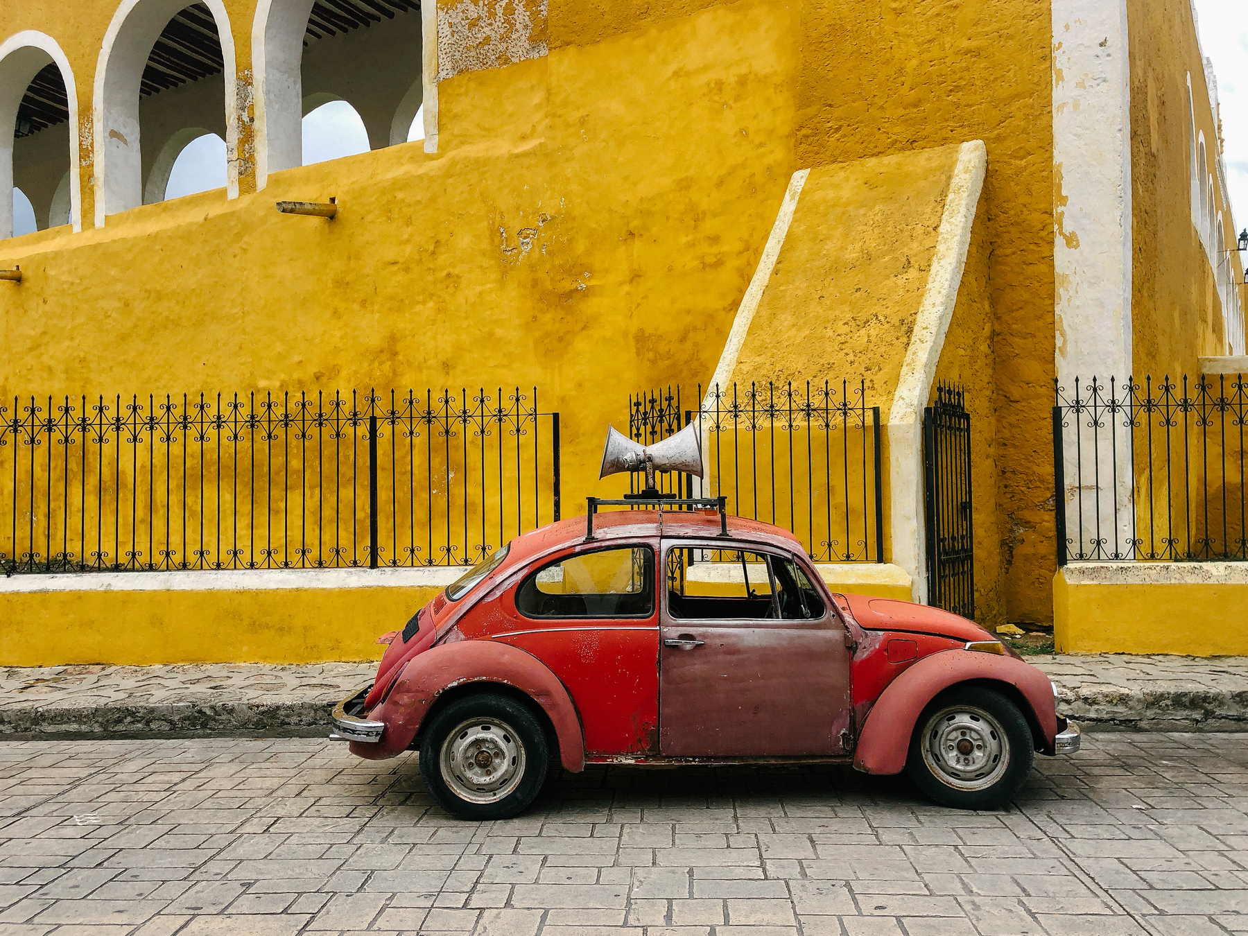 A red car parked in front of a yellow monastery.