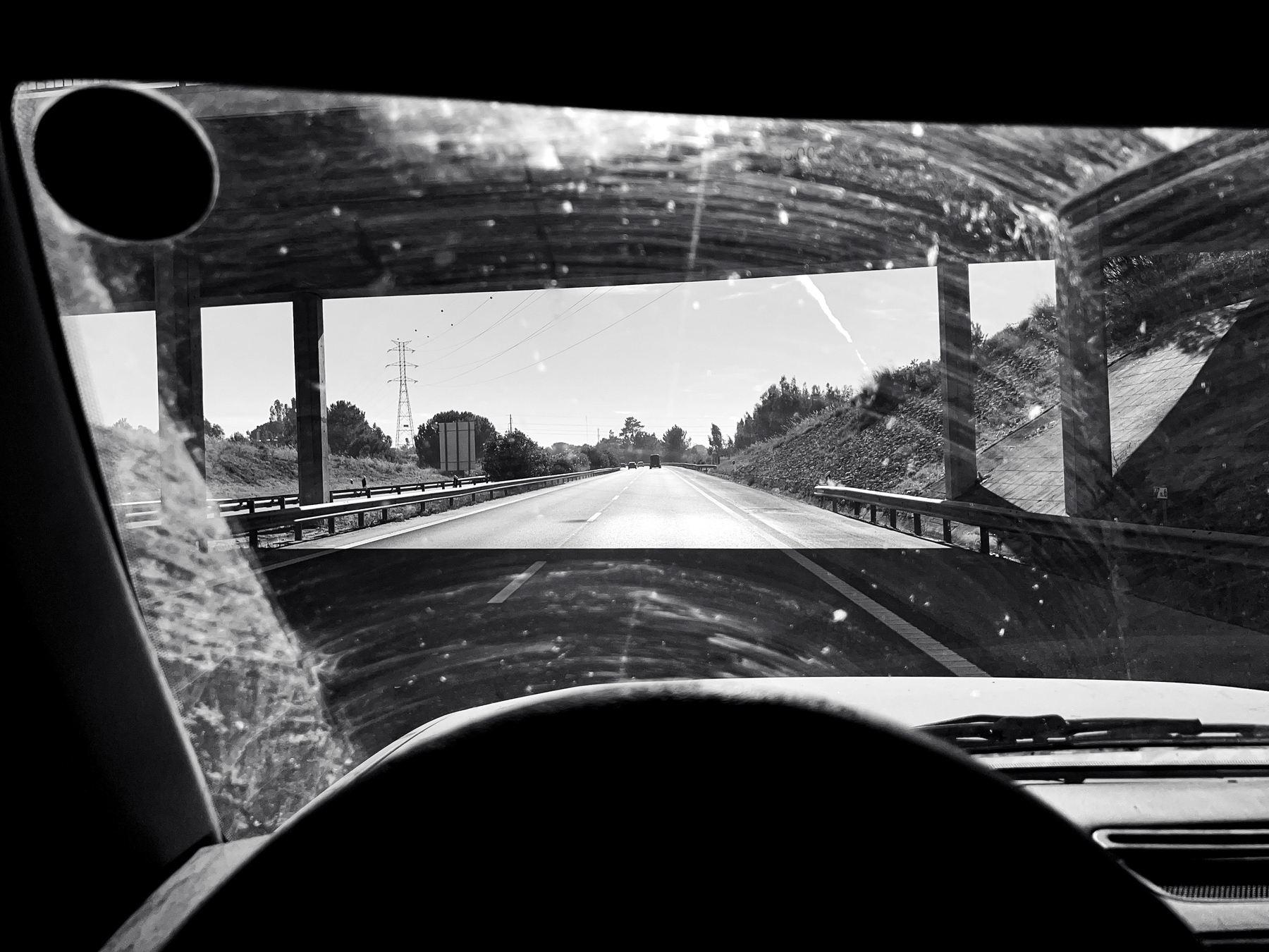 Black and white photo of a road, seen from a driver’s seat. 