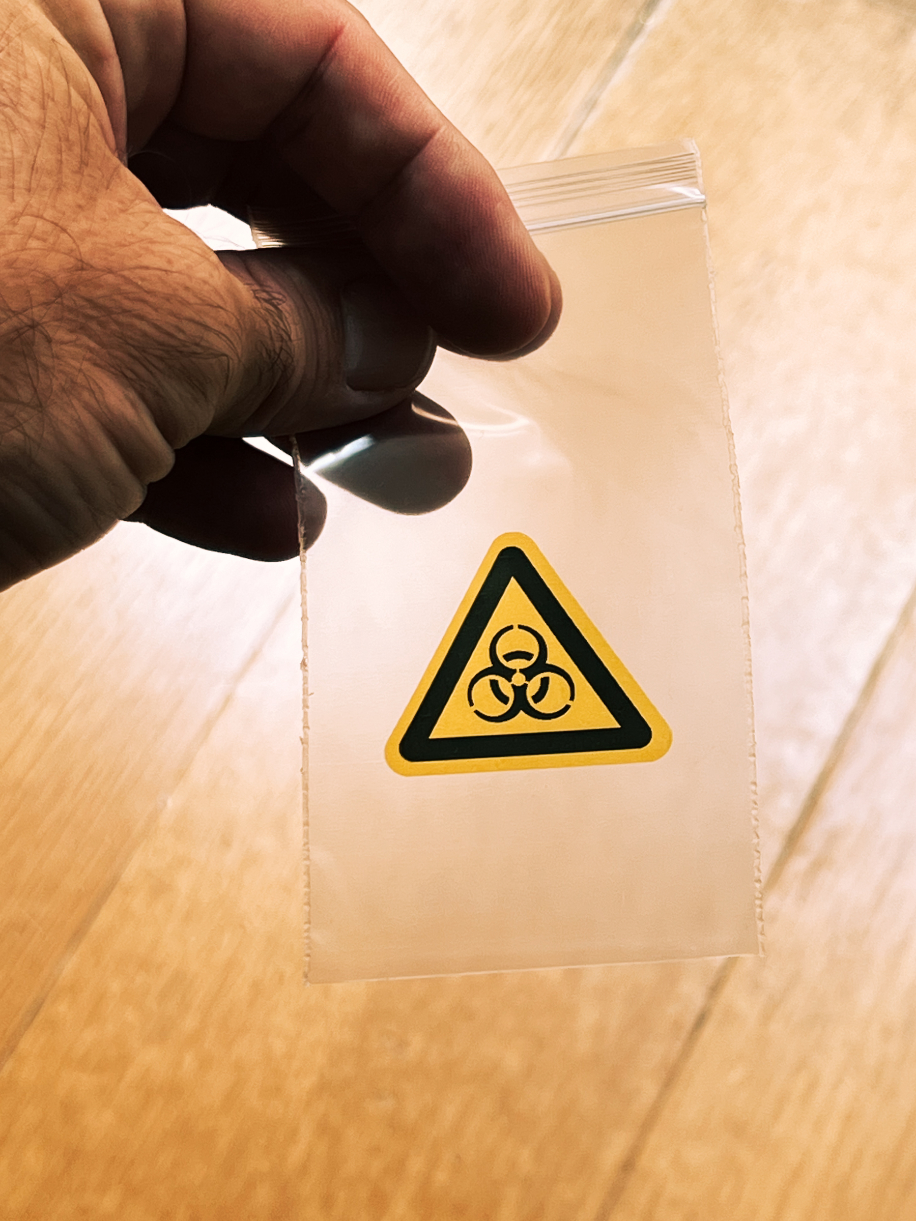 A hand holds a small plastic bag with a sign for hazardous materials.