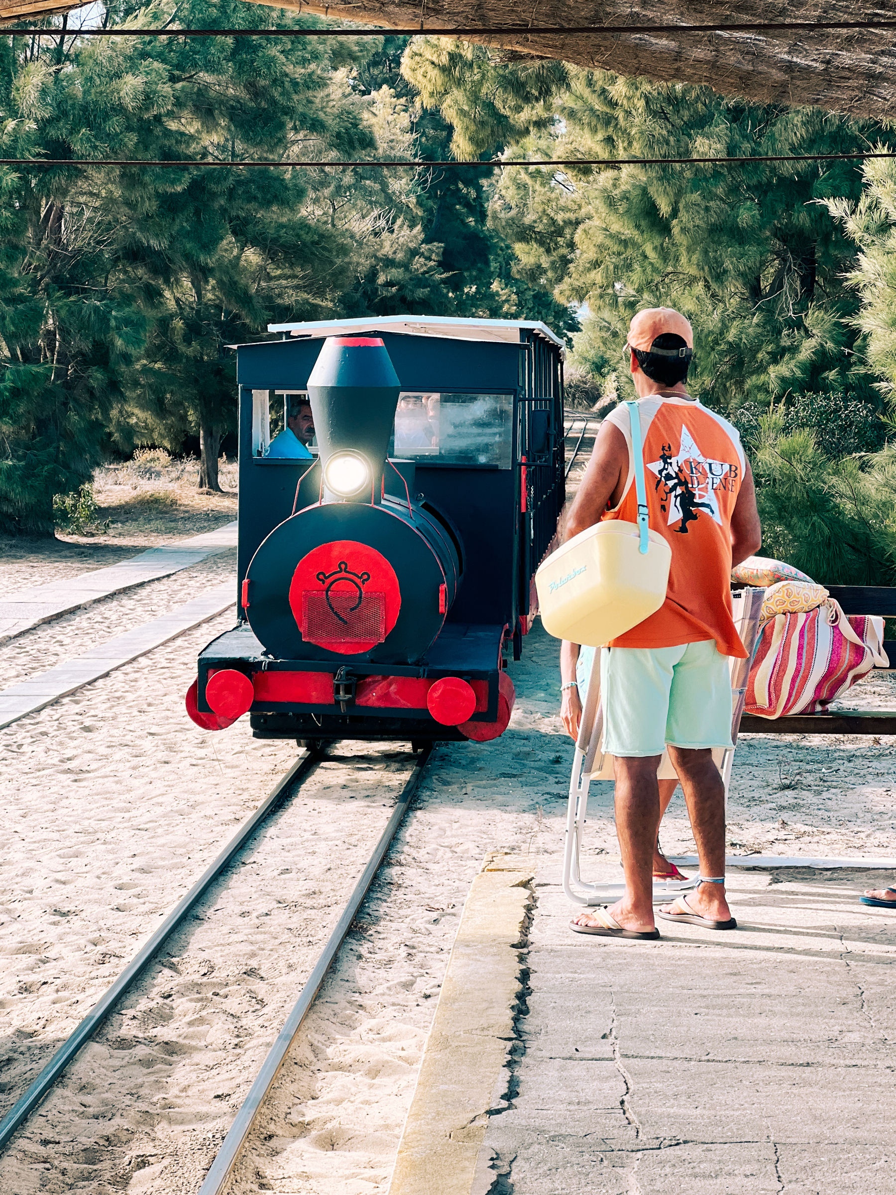 A man waits on the platform, as a very small train arrives. 