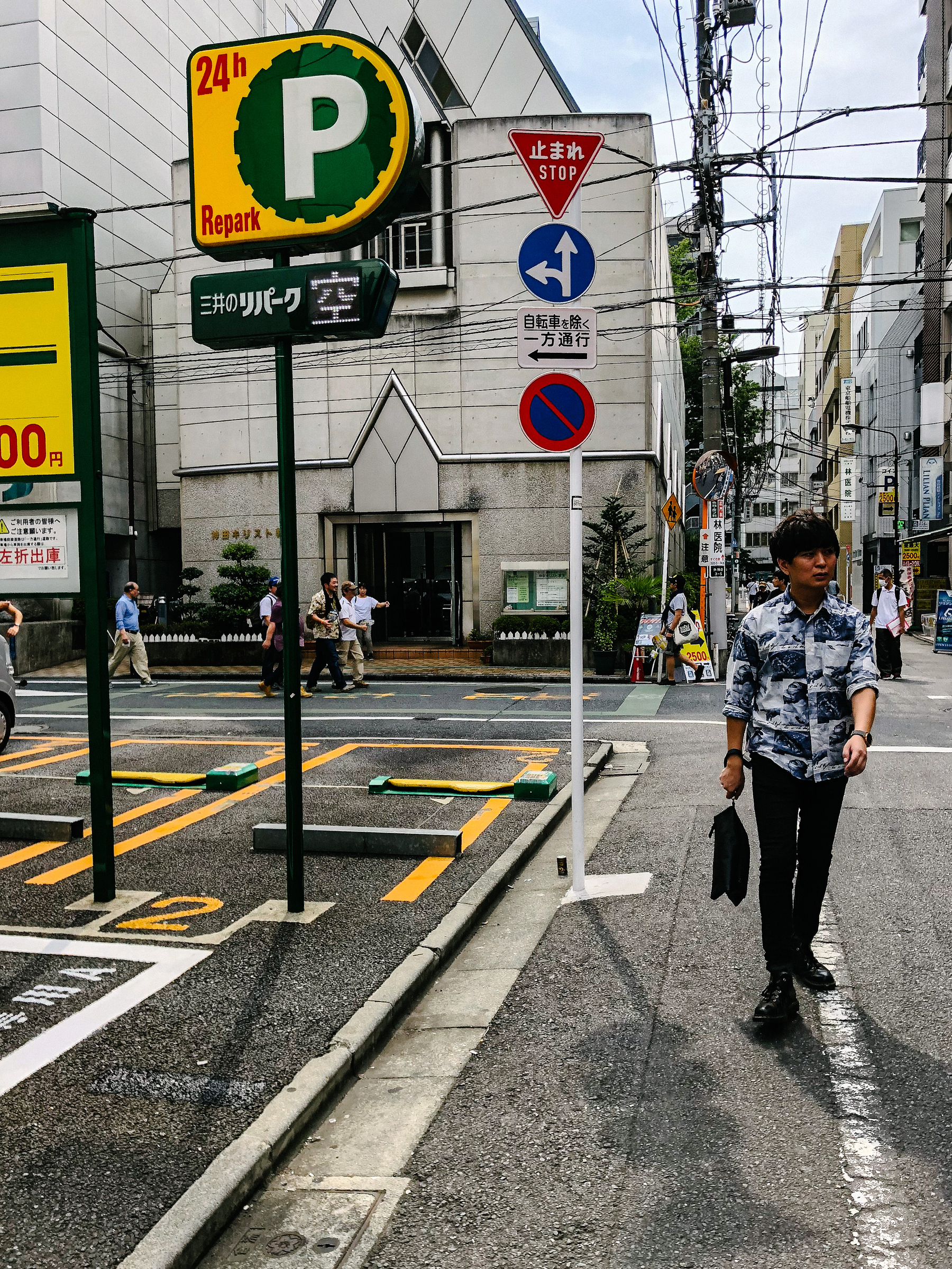 A man walks in a Tokyo street, parking spots next to him. 