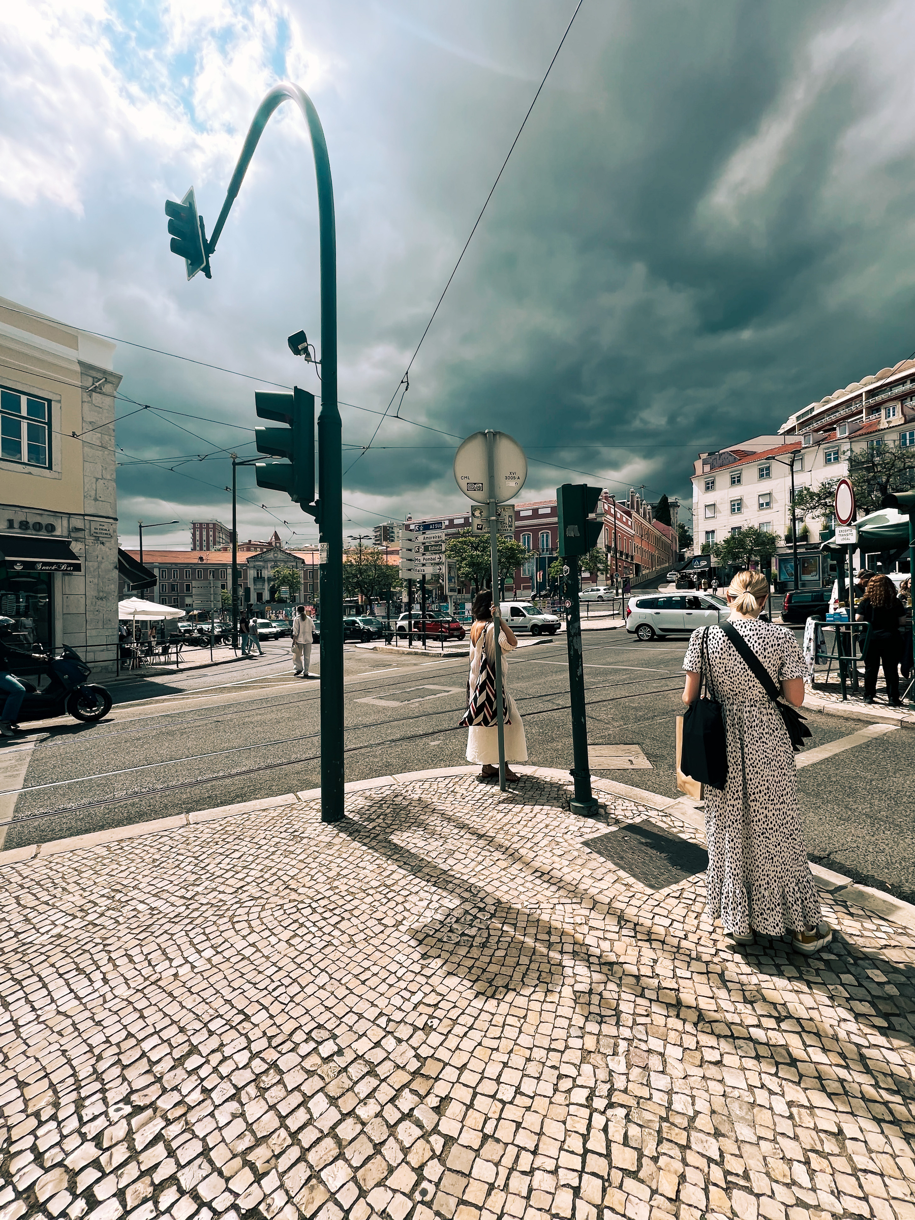 Stormy clouds over the city. A street corner, people waiting to cross. 