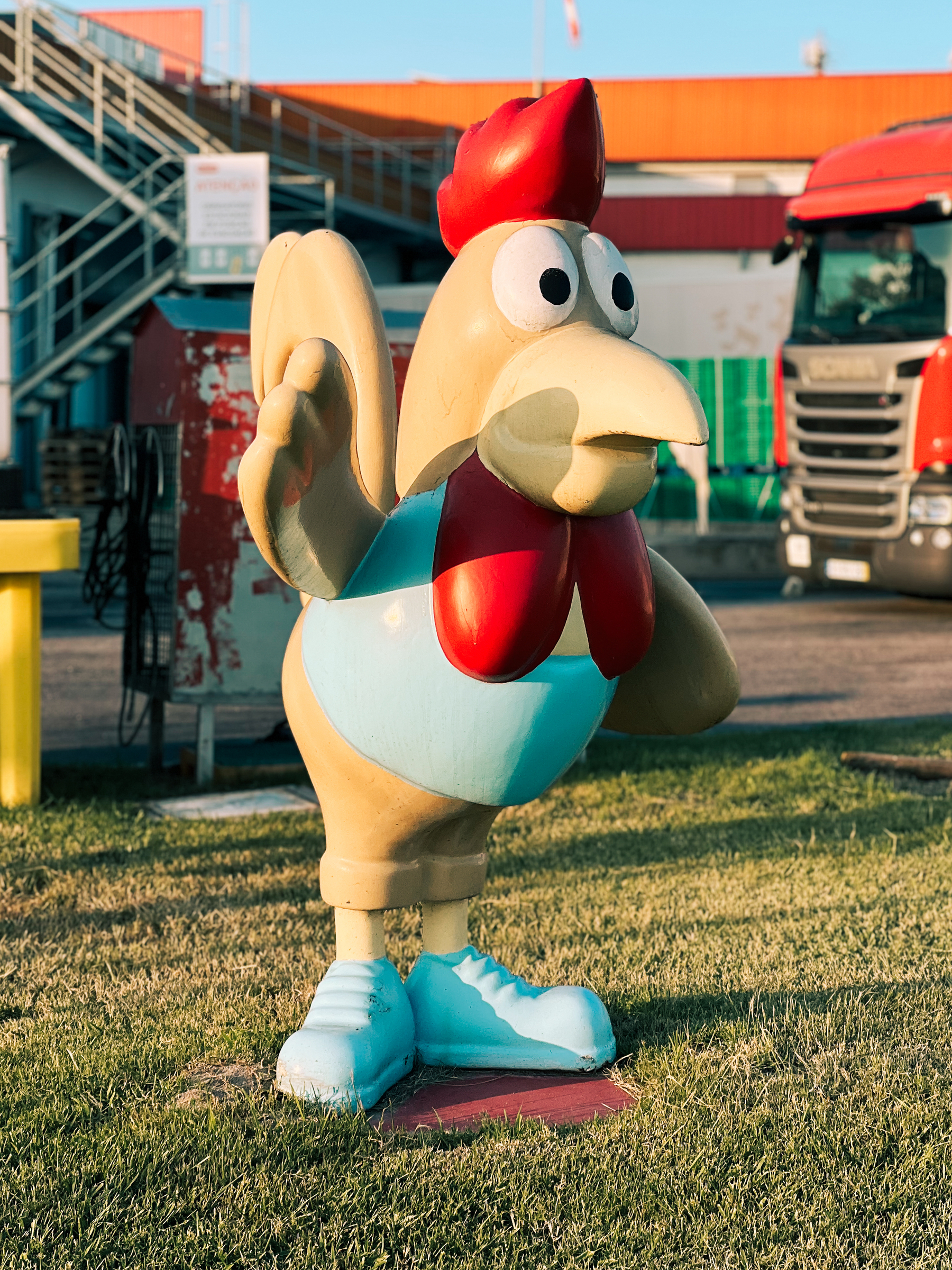 A big chicken sculpture, outside a meat processing plant. A truck can be seen in the background. 