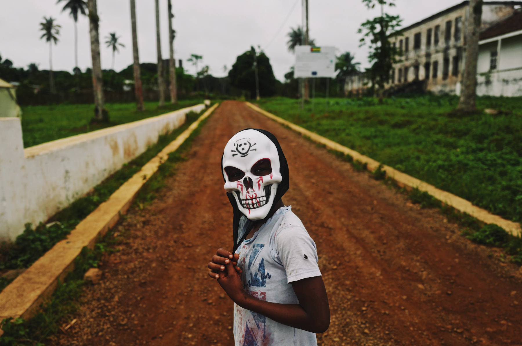 A boy stands in the middle of the road, wearing a skull mask.