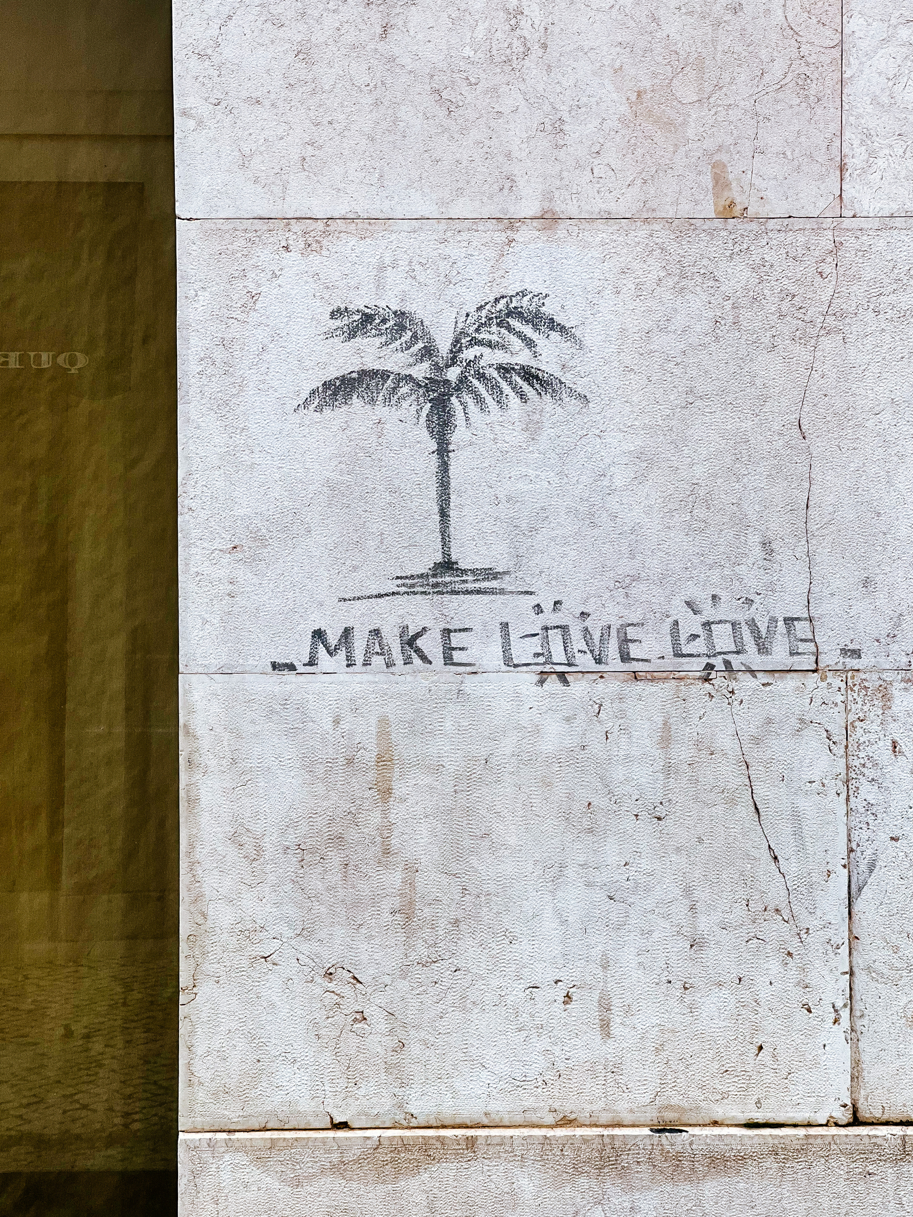 A crude palm tree is drawn on a wall, with the words “make love love”. 