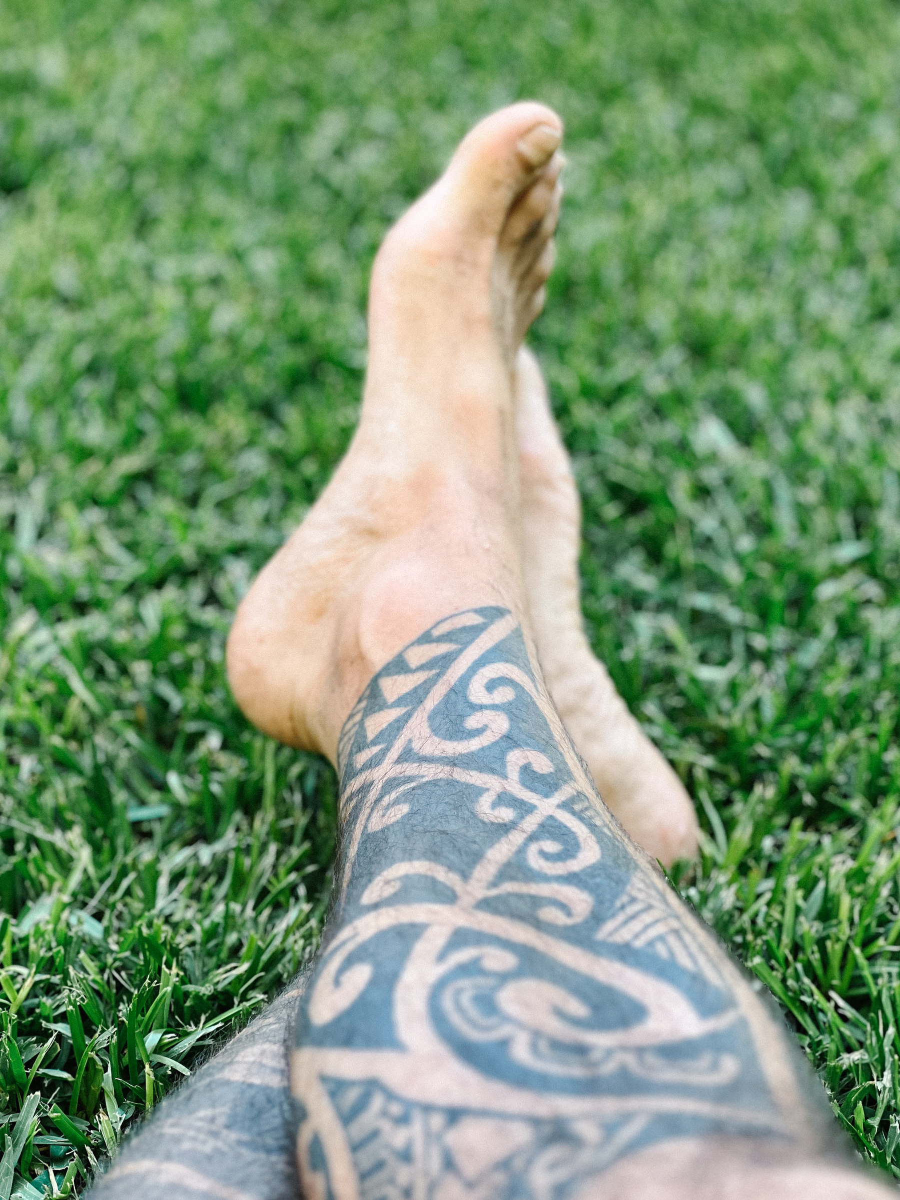 Tattooed legs, crossed, on grass.
