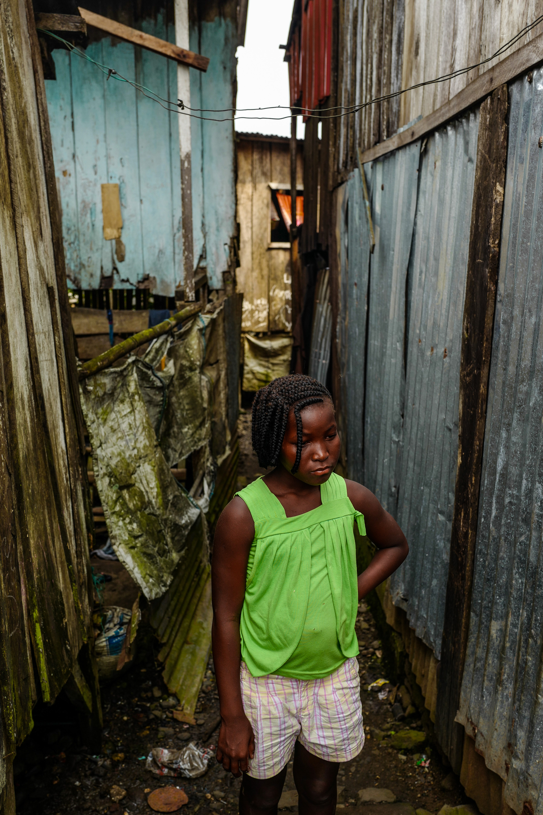 A girl stands in a tiny alley. 