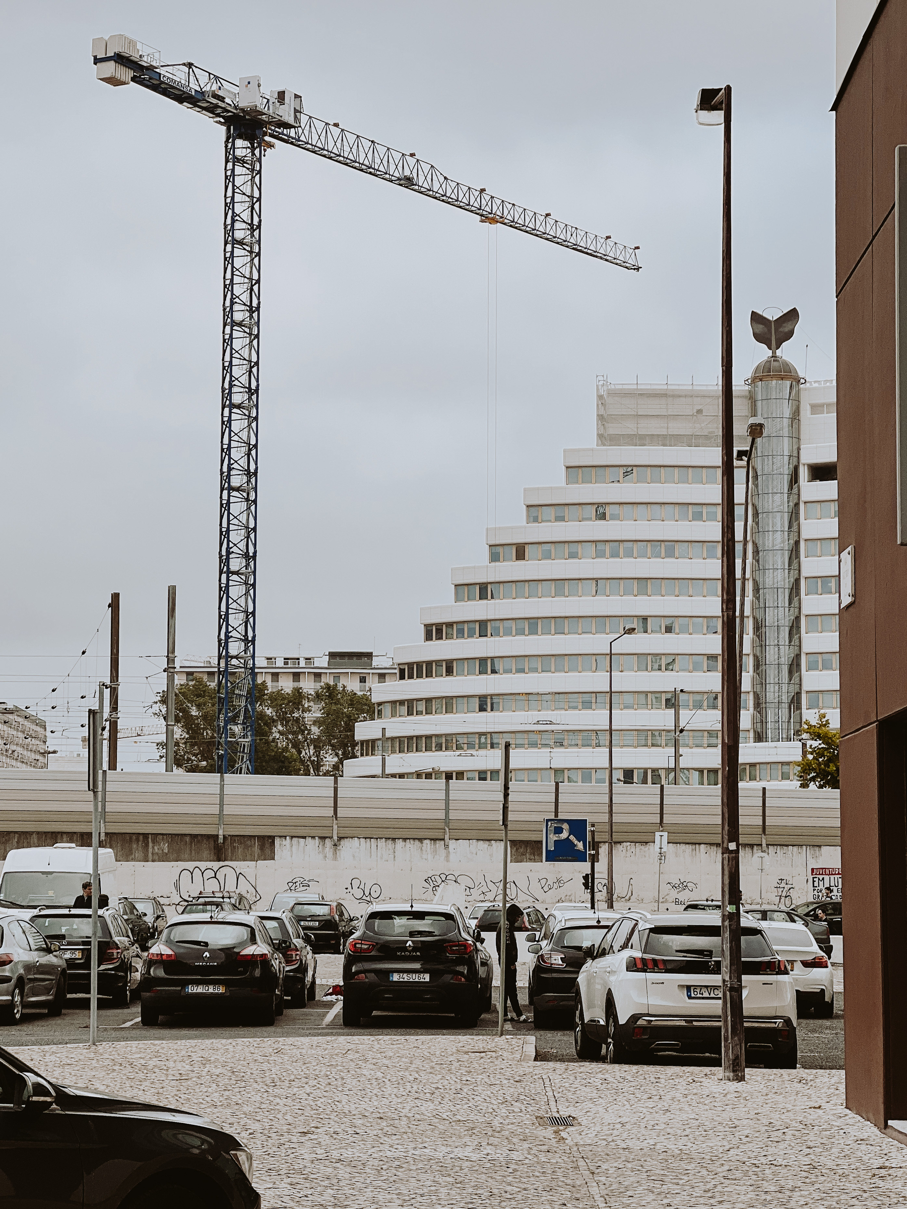 A huge crane, a building that looks like a staircase, and a car park. 