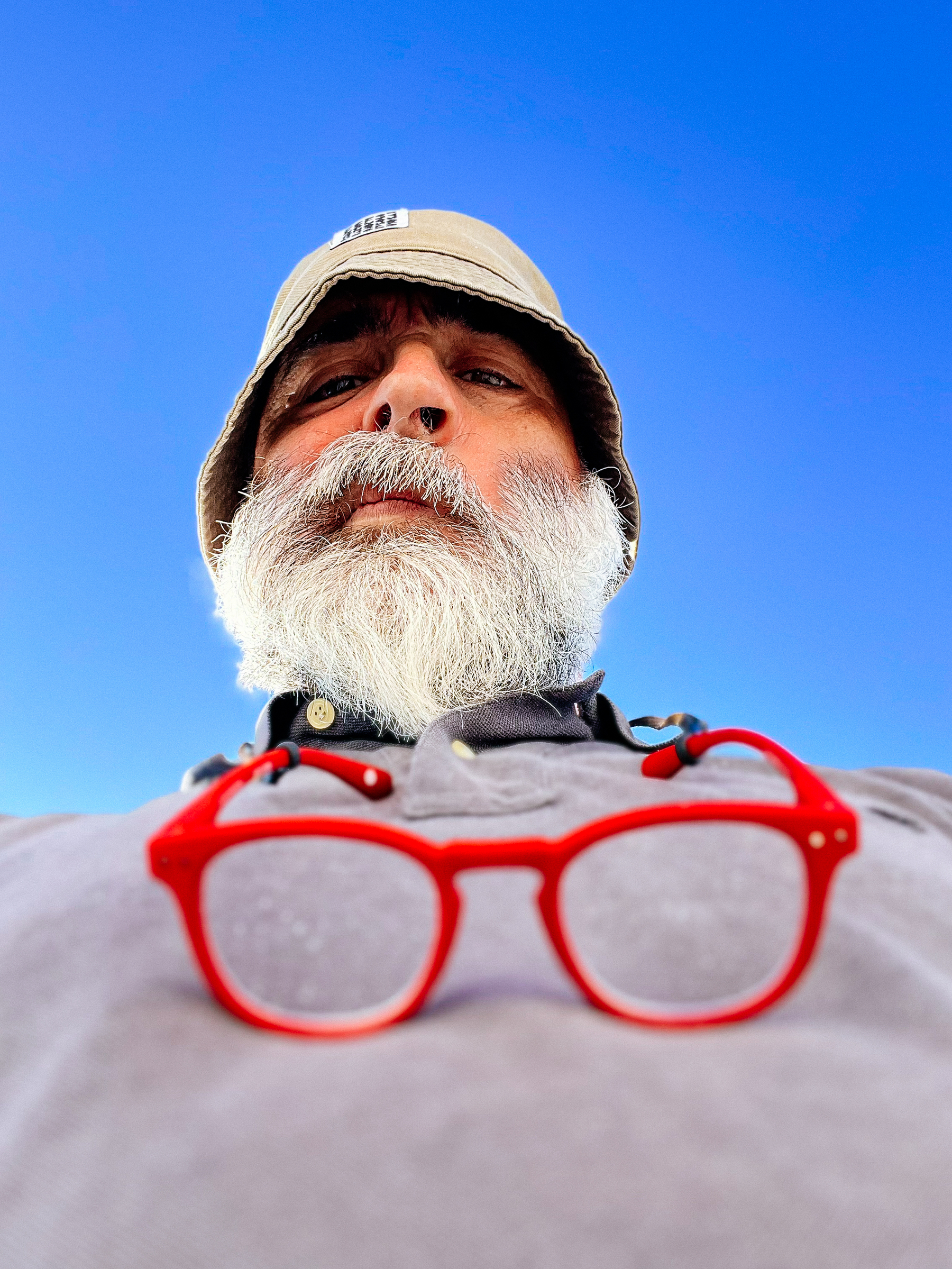 A man wearing a hat, with red glasses hanging from his neck. Photo shot from a very low angle. 