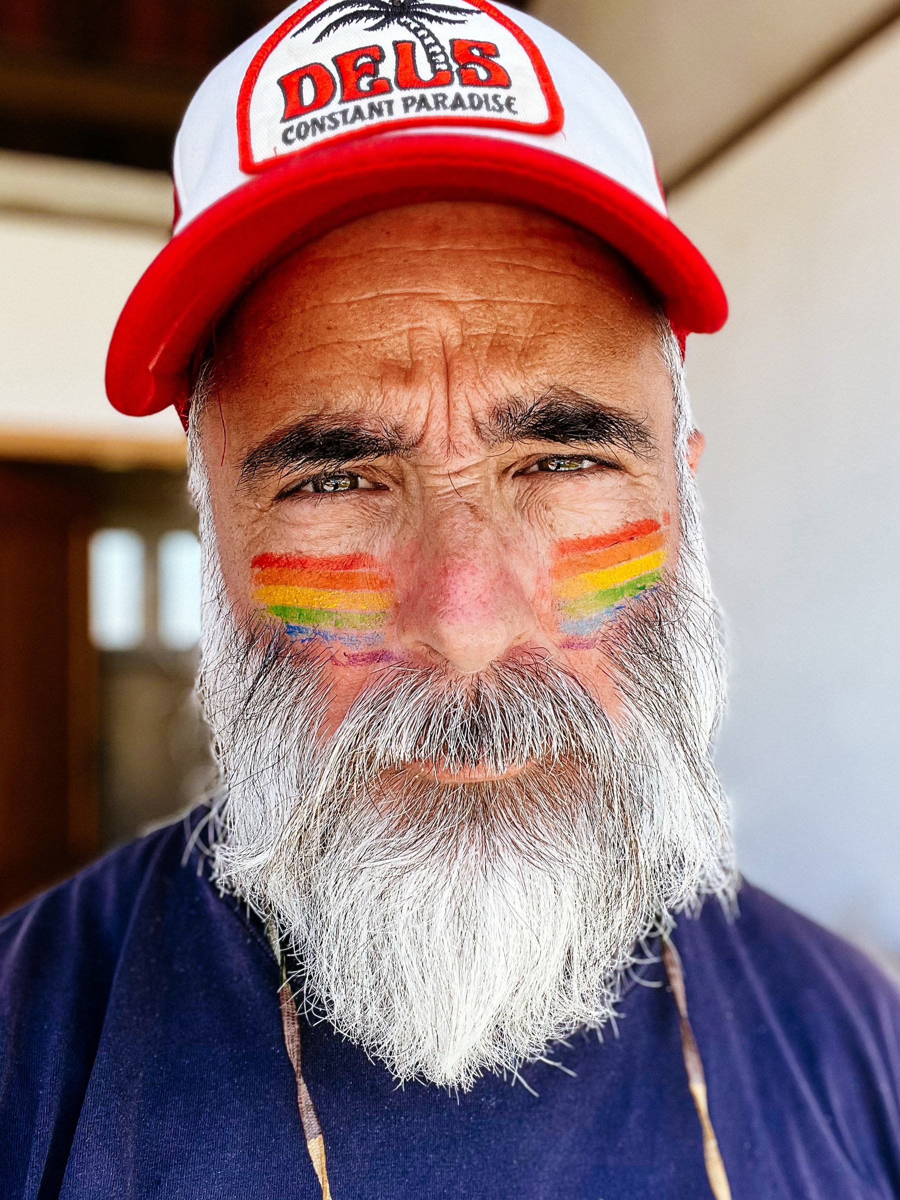A man wearing a cap, and Pride flags on his cheeks.