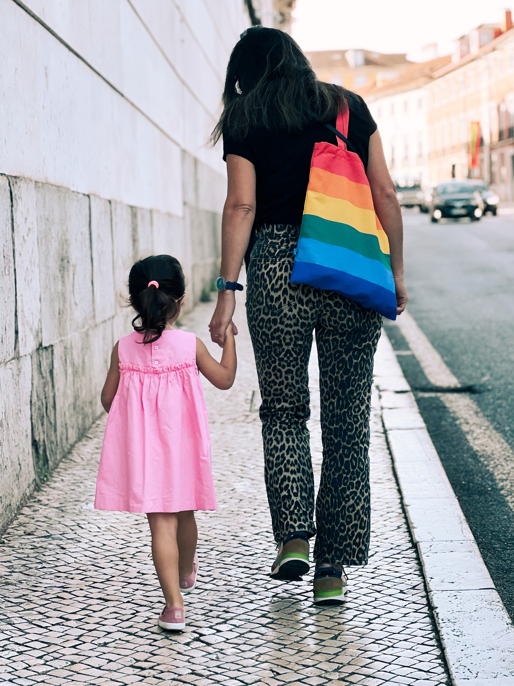A woman and a child walk hand in hand. The woman has a rainbow colored tote. 