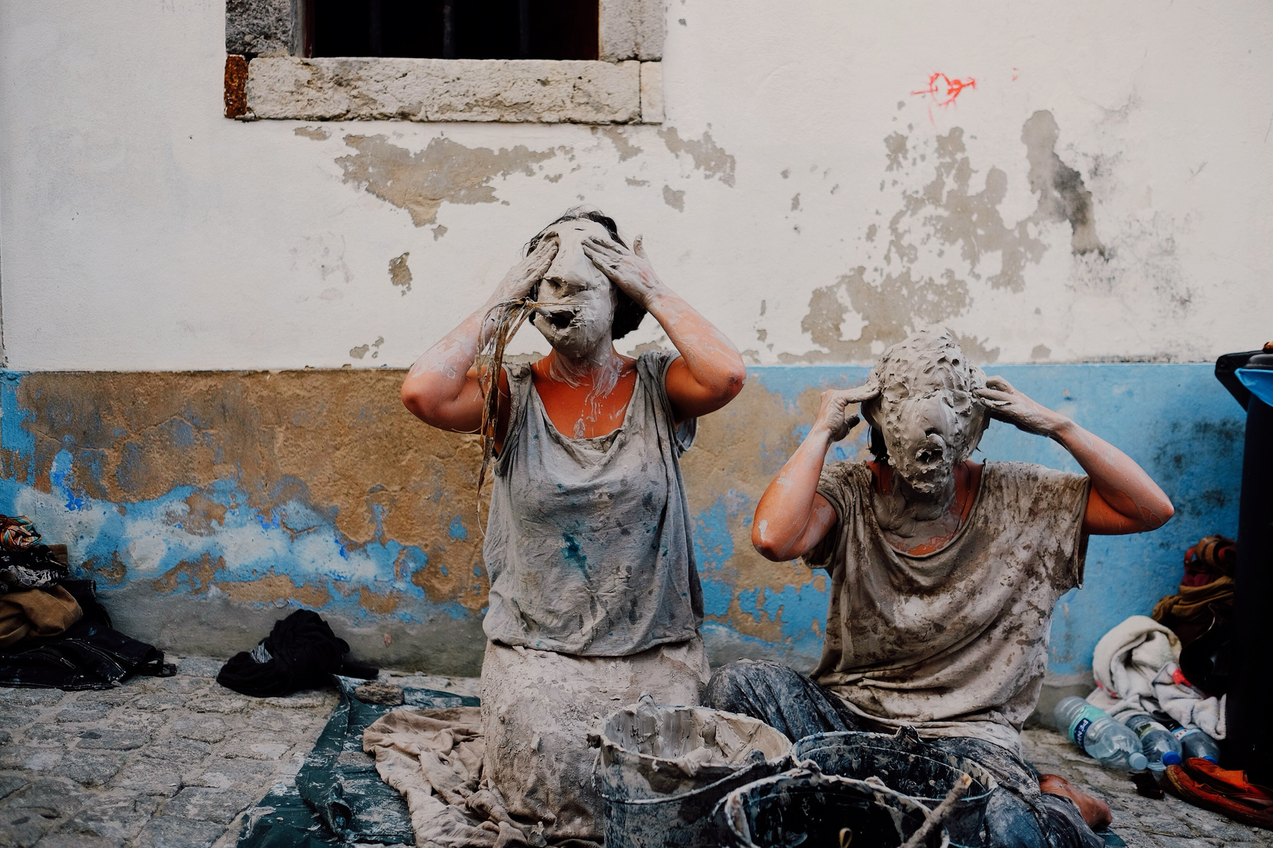 Two street performers cover their faces with mud. 